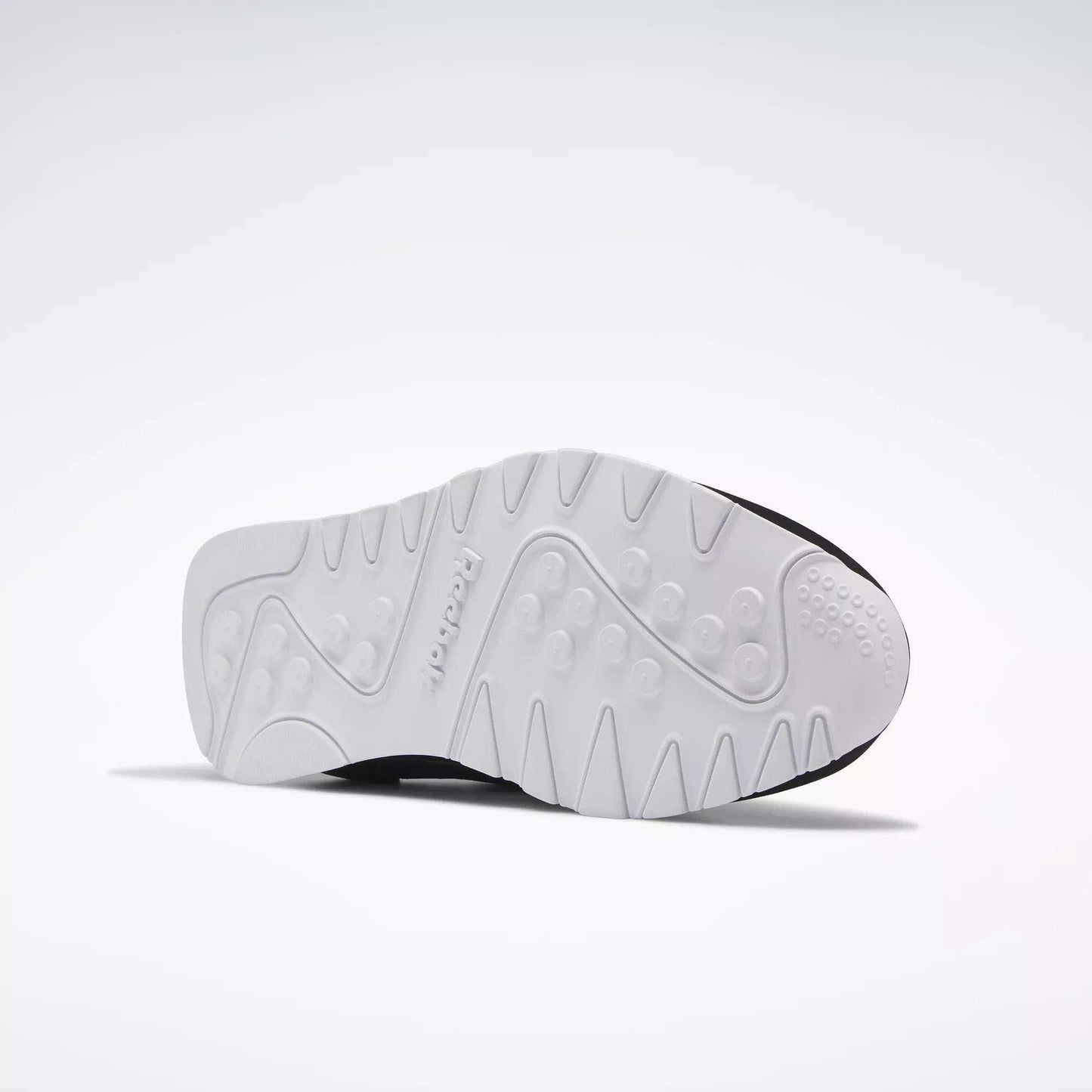 The image displays the white, textured sole of Reebok Men's Classic Nylon Shoes with circular grips and patterns—an excellent everyday sneaker—set against a plain, light background.