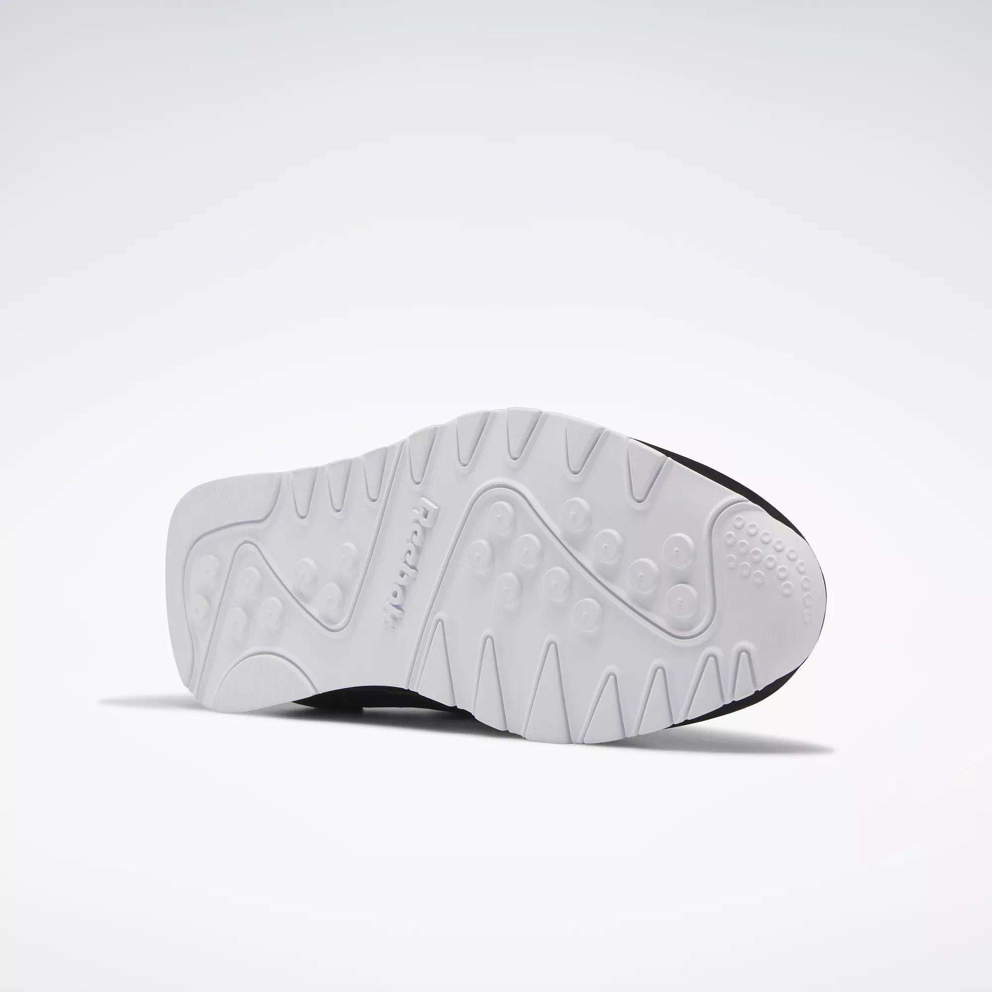 The image displays the white, textured sole of Reebok Men's Classic Nylon Shoes with circular grips and patterns—an excellent everyday sneaker—set against a plain, light background.