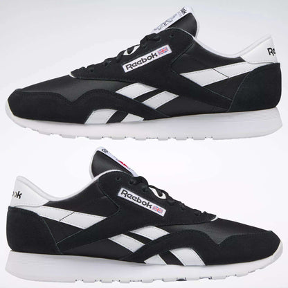 Two black Reebok Men's Classic Nylon Shoes with white soles and side stripes are shown side by side on a plain background. The Reebok logo and a small UK flag appear on the sides and tongue of these classic sneakers.