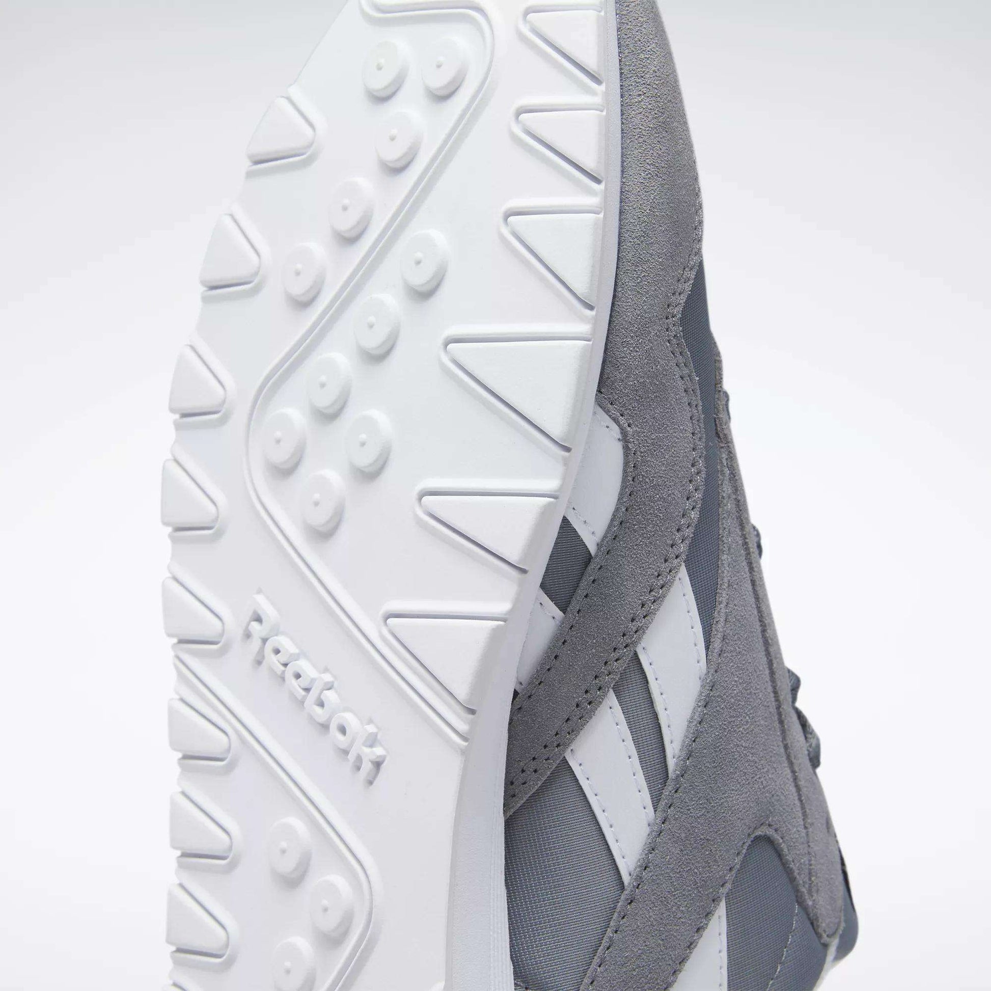 Close-up of the underside of Reebok Men's Classic Nylon Shoes in gray and white, highlighting the textured white rubber sole with Reebok logo, gray nylon upper, and iconic side stripes—timeless sneakers for everyday wear.