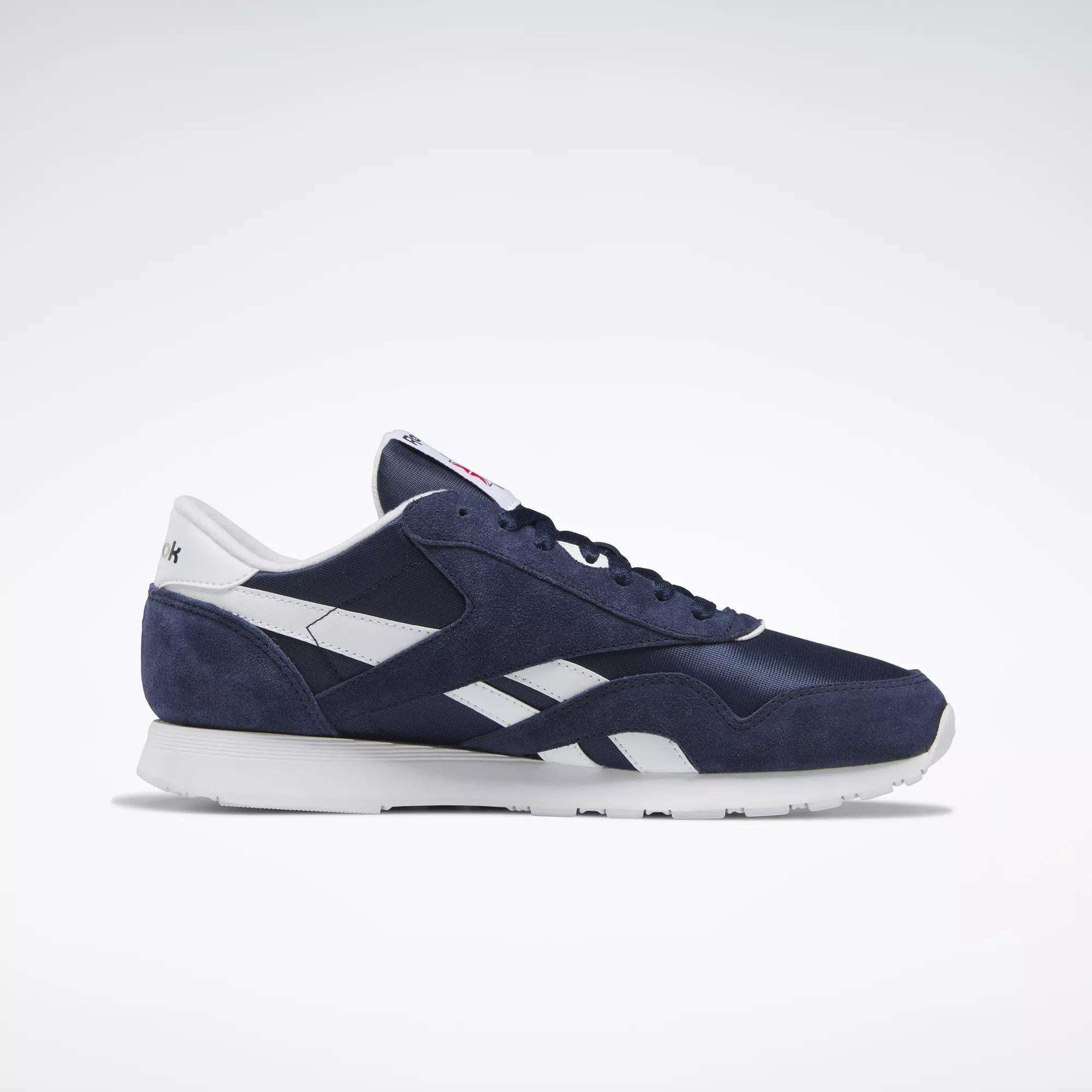 The Reebok Men's Classic Nylon Shoes feature a navy blue and white design, nylon upper, white sole, bold side logo, and timeless everyday sneaker style—displayed in side profile against a plain light background.