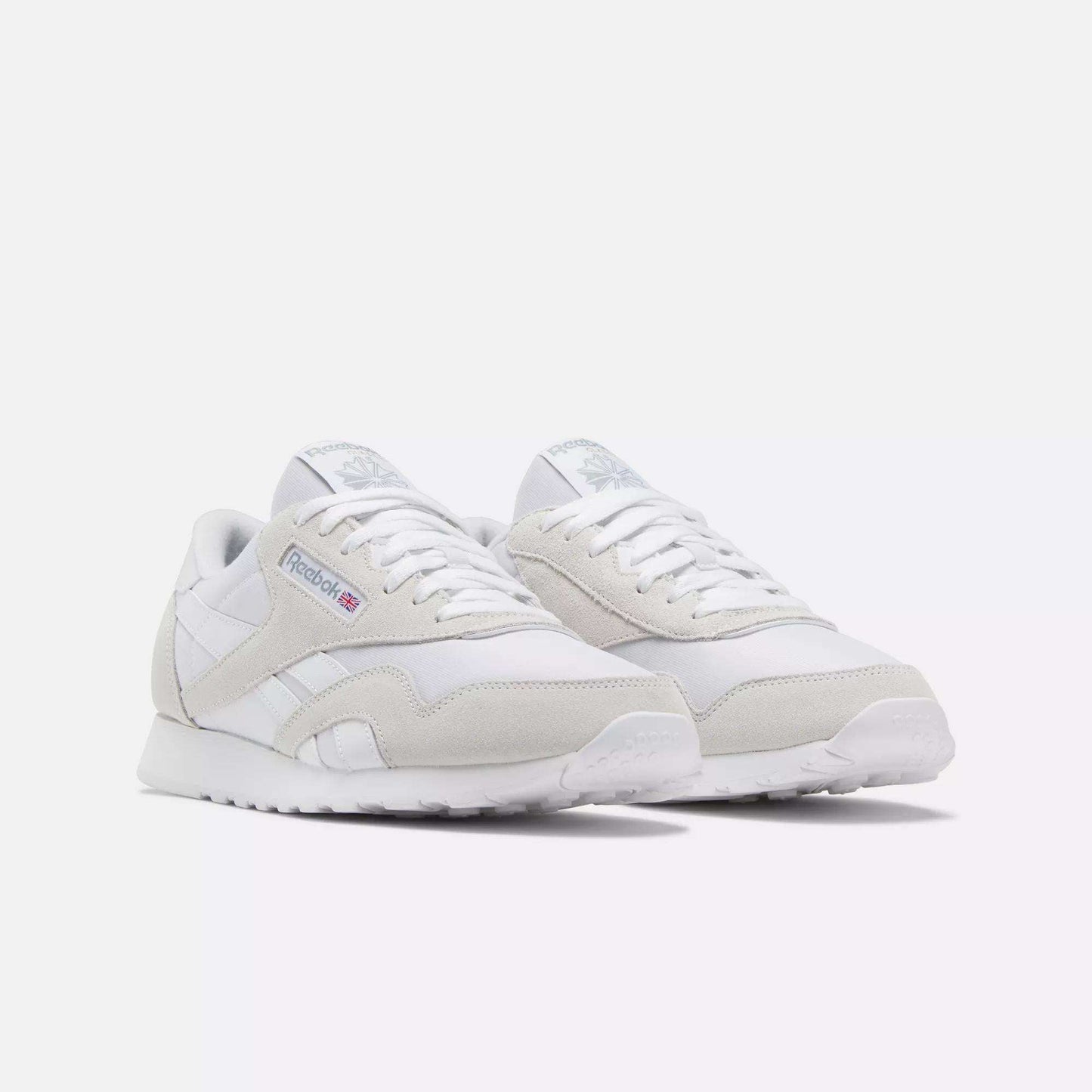 The Reebok Men's Classic Nylon Shoes feature white uppers with light gray suede accents, white laces, and the iconic Reebok logo on the side—perfect everyday sneakers for a clean, classic look.