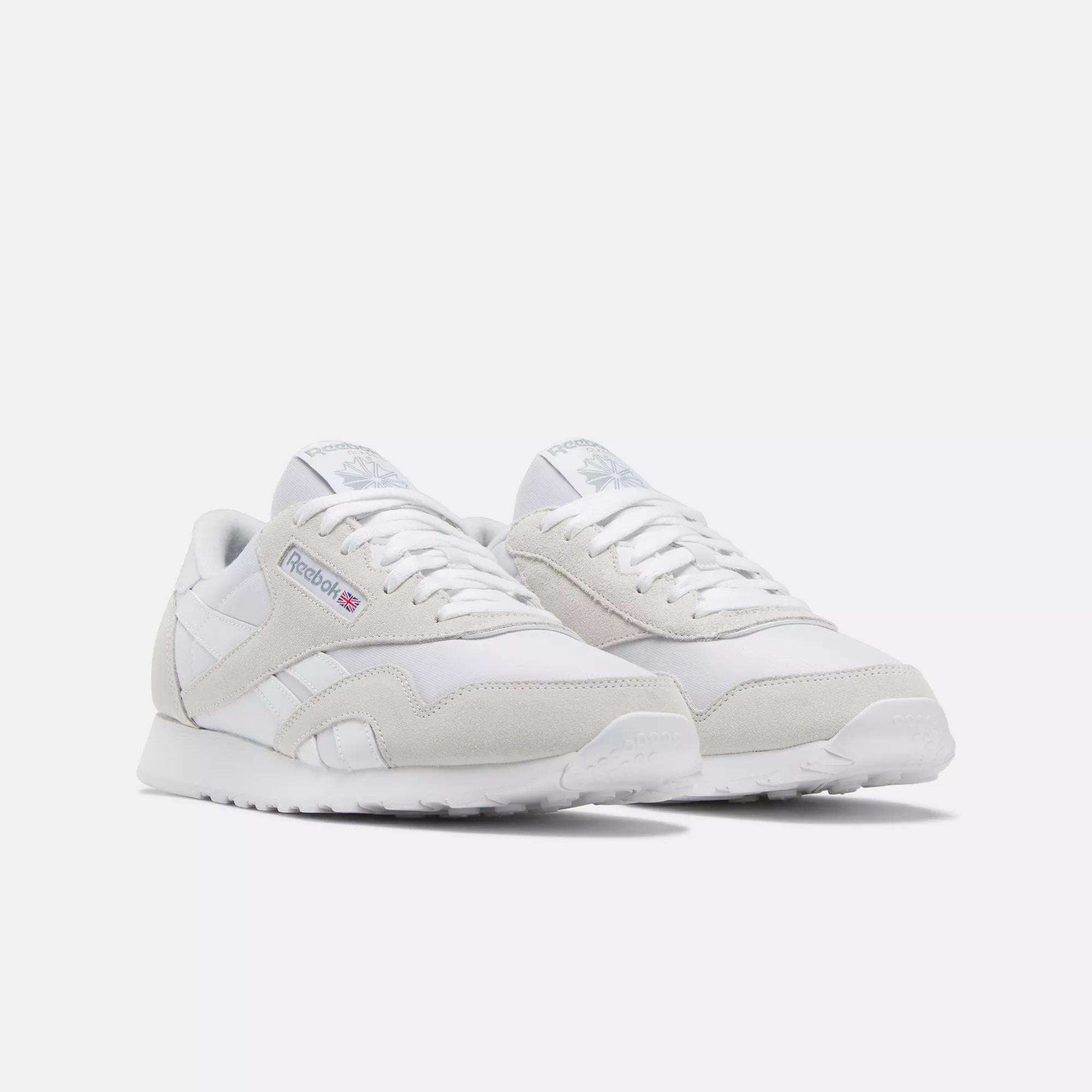 The Reebok Men's Classic Nylon Shoes feature white uppers with light gray suede accents, white laces, and the iconic Reebok logo on the side—perfect everyday sneakers for a clean, classic look.