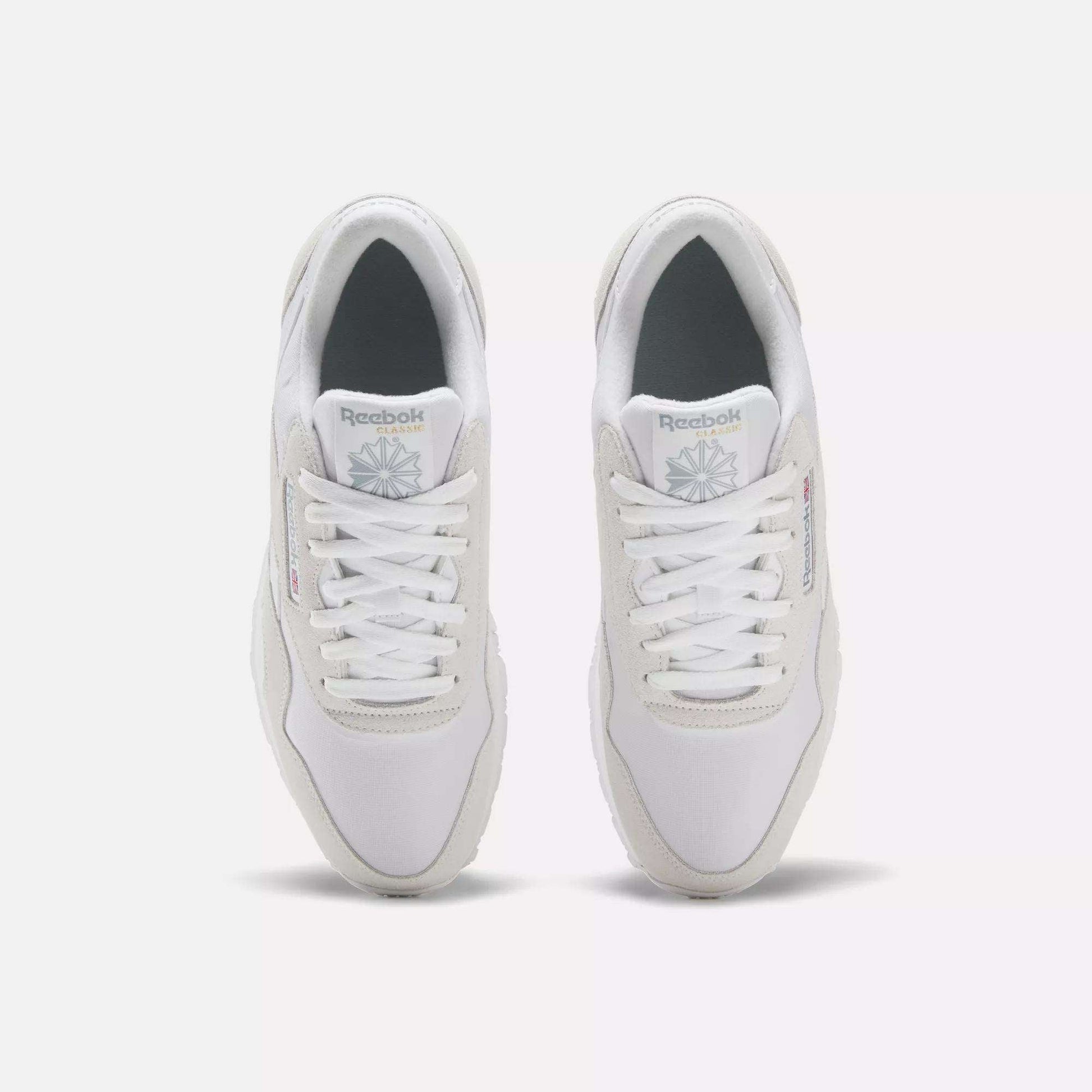 A pair of Men's Classic Nylon Shoes by Reebok in white, seen from above with white laces, light gray accents, and the Reebok logo on the tongue and side—timeless sneakers set side by side on a plain white background.