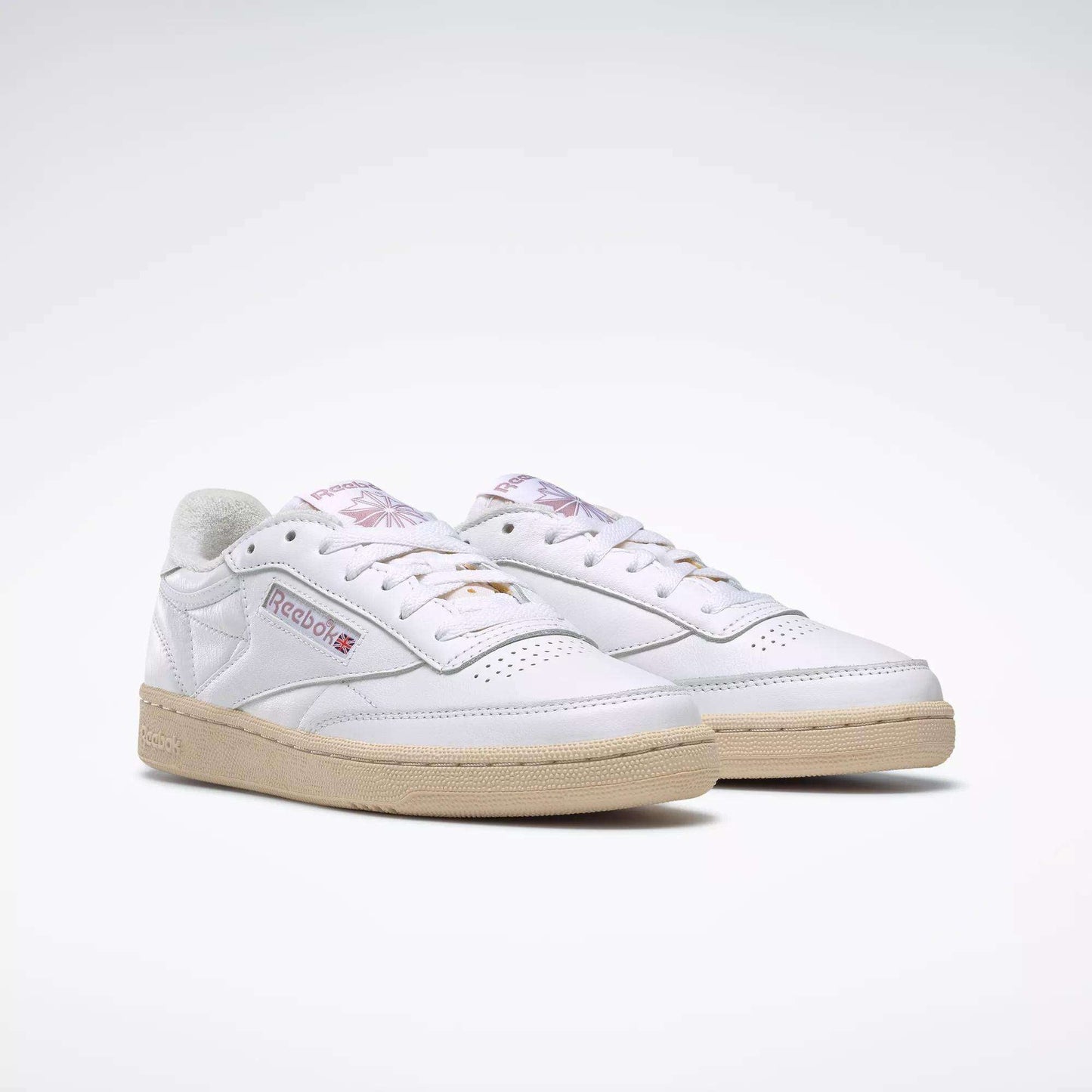 The Reebok Women's Club C 85 Vintage Shoes feature white uppers, beige soles, a side Reebok logo patch, and subtle purple detailing on the tongue, shown against a plain white background.