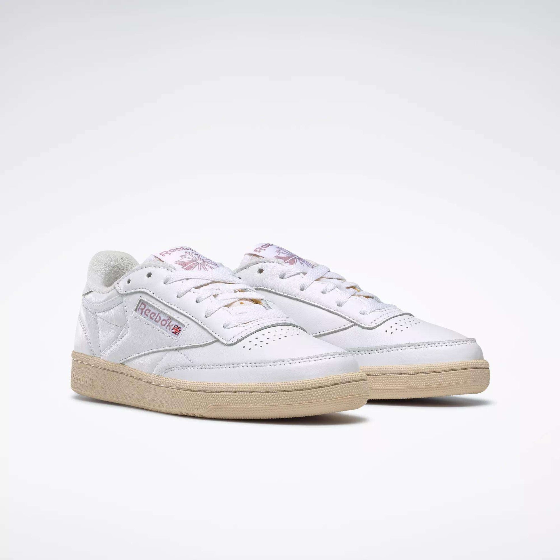 The Reebok Women's Club C 85 Vintage Shoes feature white uppers, beige soles, a side Reebok logo patch, and subtle purple detailing on the tongue, shown against a plain white background.