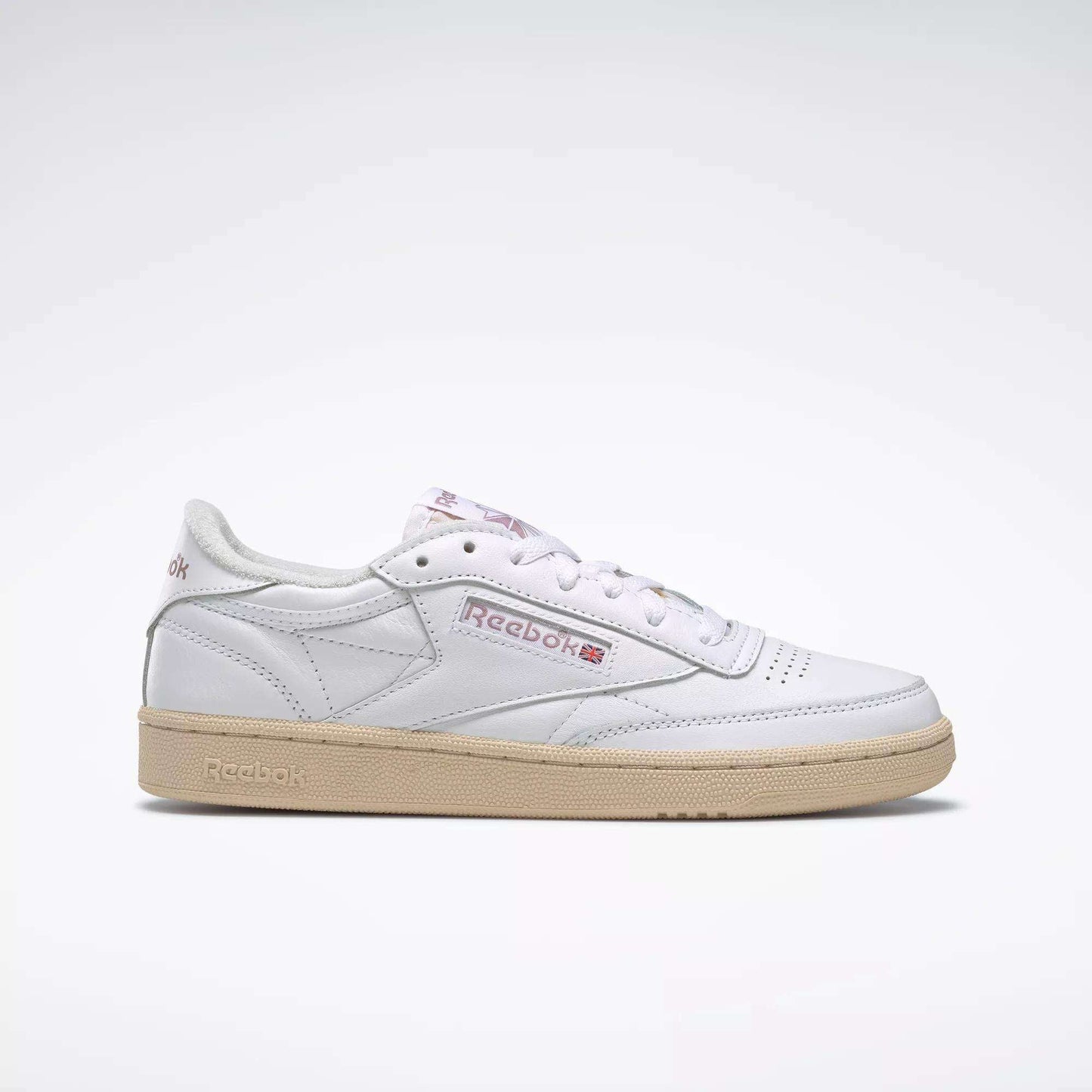 A side view of a white Reebok Women's Club C 85 Vintage Shoe with a beige sole, featuring the Reebok logo and Union Jack on the side, set against a plain light gray background.