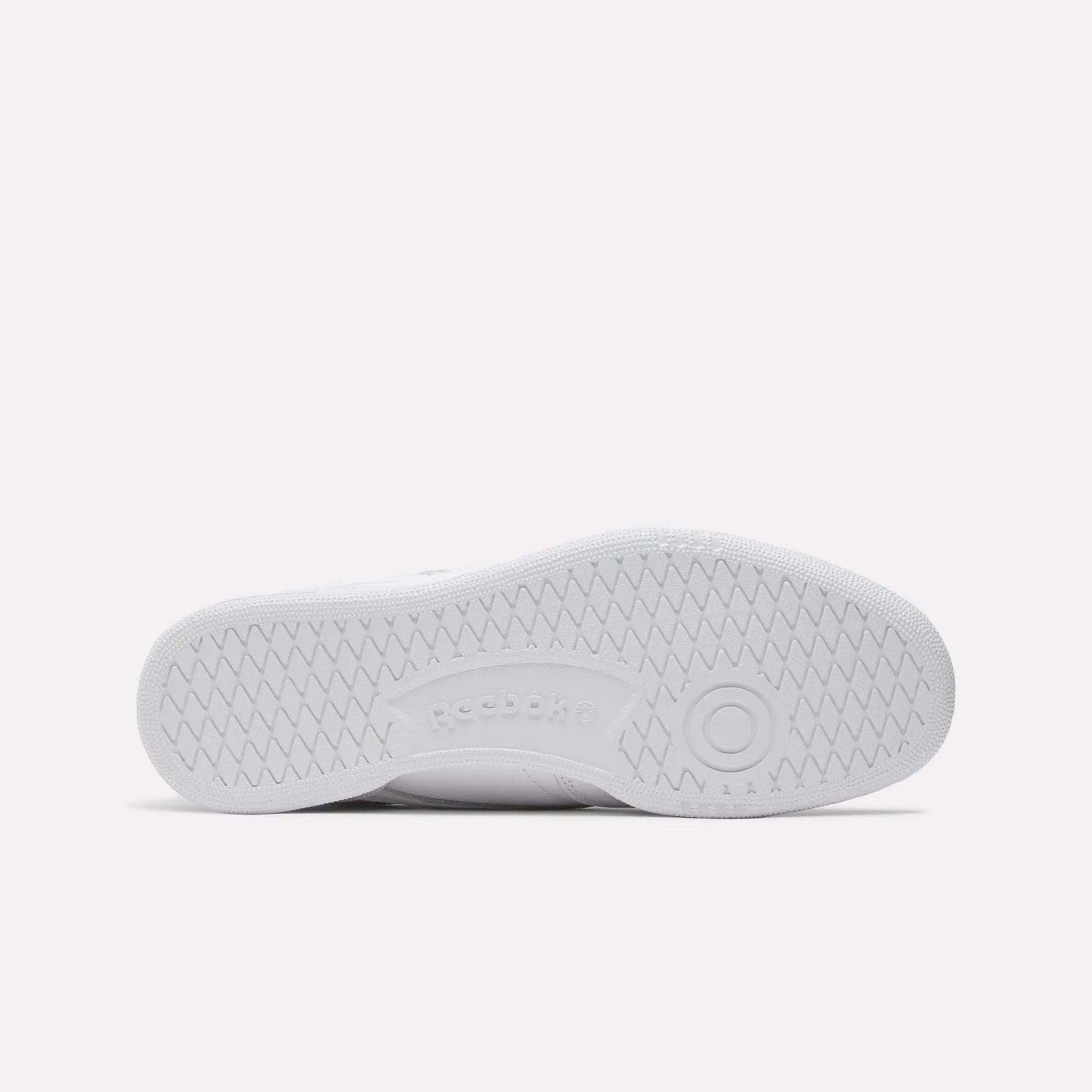 The image displays the bottom view of a Reebok Club C 85 Shoes sole, featuring a white herringbone tread pattern and center-embossed Reebok logo, emphasizing its classic tennis-inspired design.