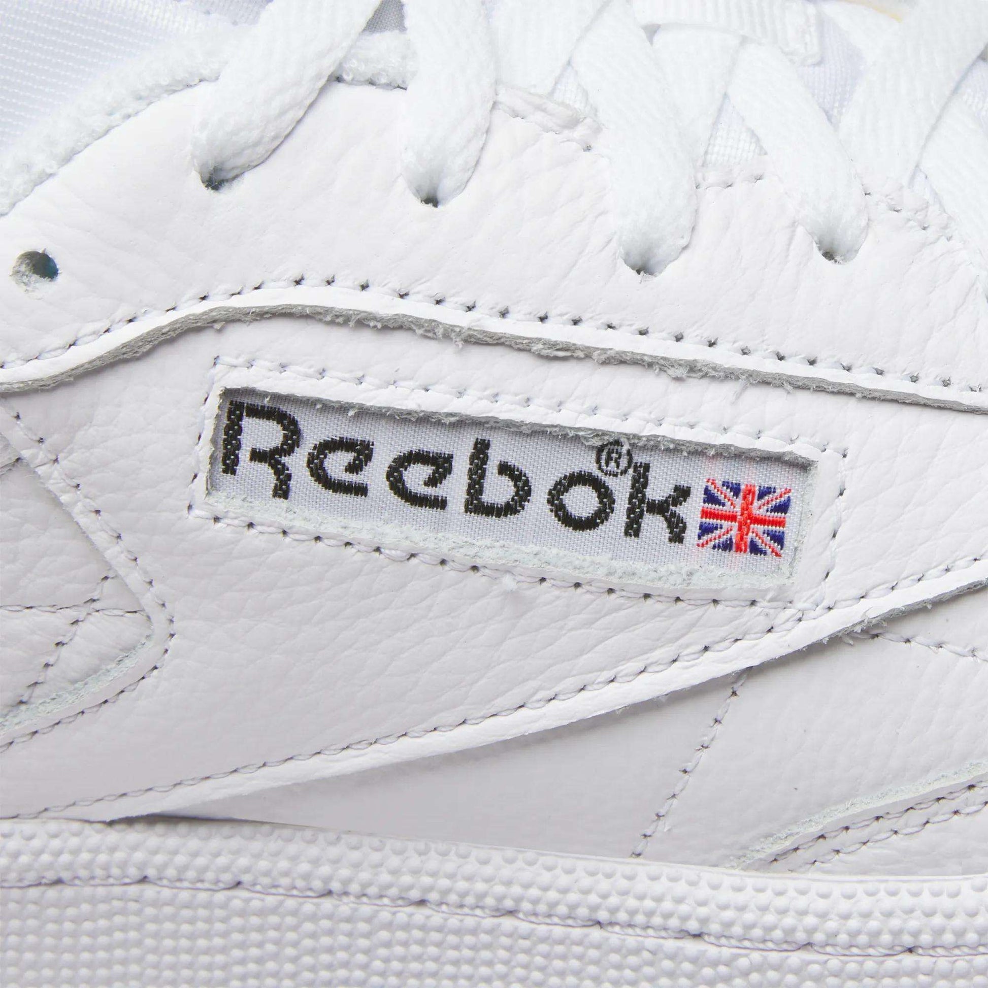 Close-up of Reebok Men's Club C 85 Shoes, featuring the stitched logo and Union Jack flag on the side, with visible leather texture and white laces.