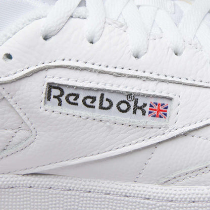 Close-up of Reebok Men's Club C 85 Shoes, featuring the stitched logo and Union Jack flag on the side, with visible leather texture and white laces.