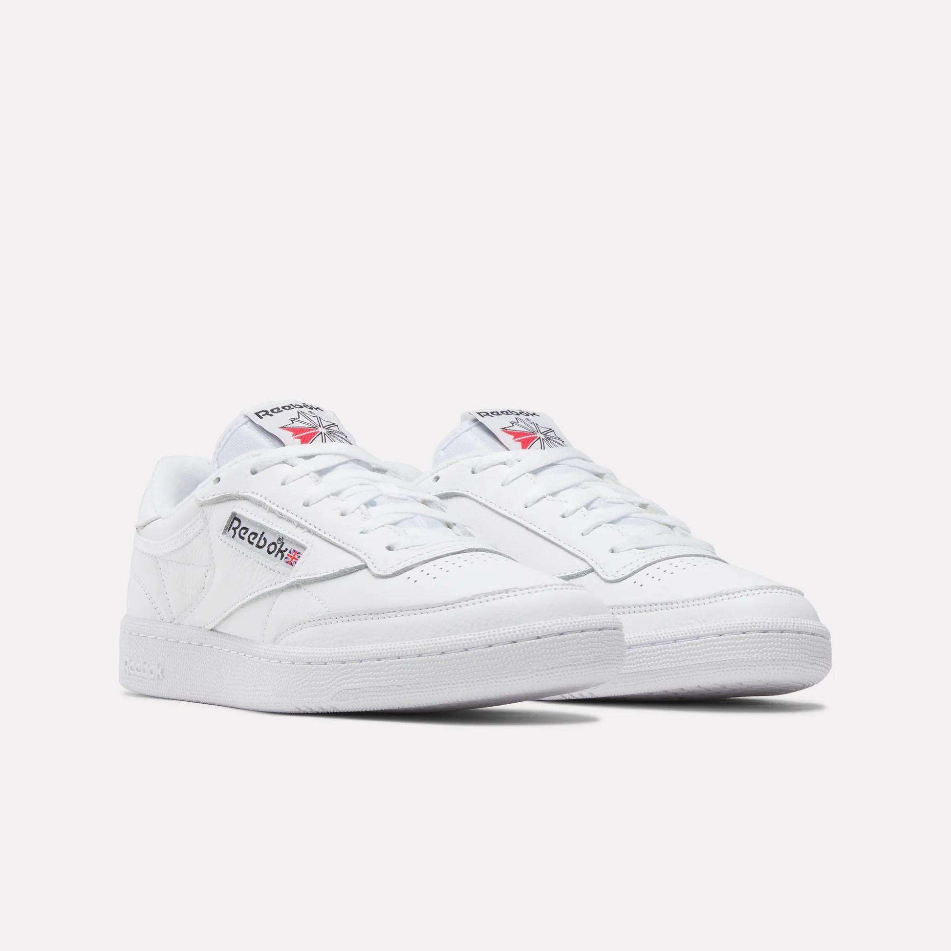 A pair of Reebok Club C 85 Shoes in white leather with low tops, showing the Reebok logo and Union Jack on the side. Inspired by classic tennis styles, displayed against a plain white background.