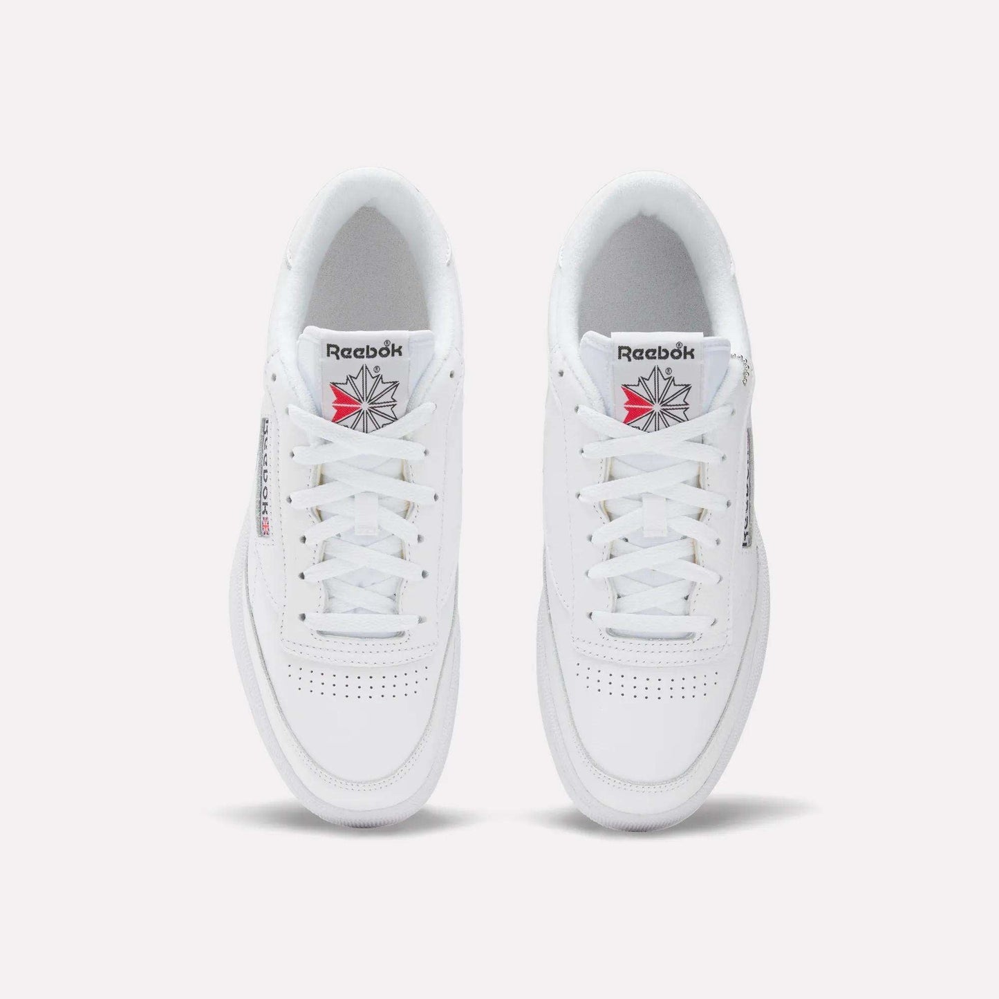 A top view of the Reebok Club C 85 Shoes in white leather, showcasing tennis-inspired toe perforations, white laces, and the Reebok logo with a red and gray starburst on the tongue.