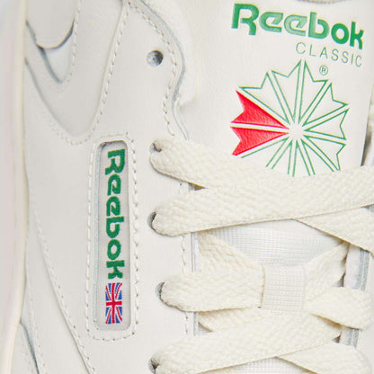 Close-up of Reebok Women's Club C Extra Shoes in white, highlighting the green Reebok logo, red and green star emblem, white laces, an embroidered Union Jack flag, and a modern platform midsole designed for women.