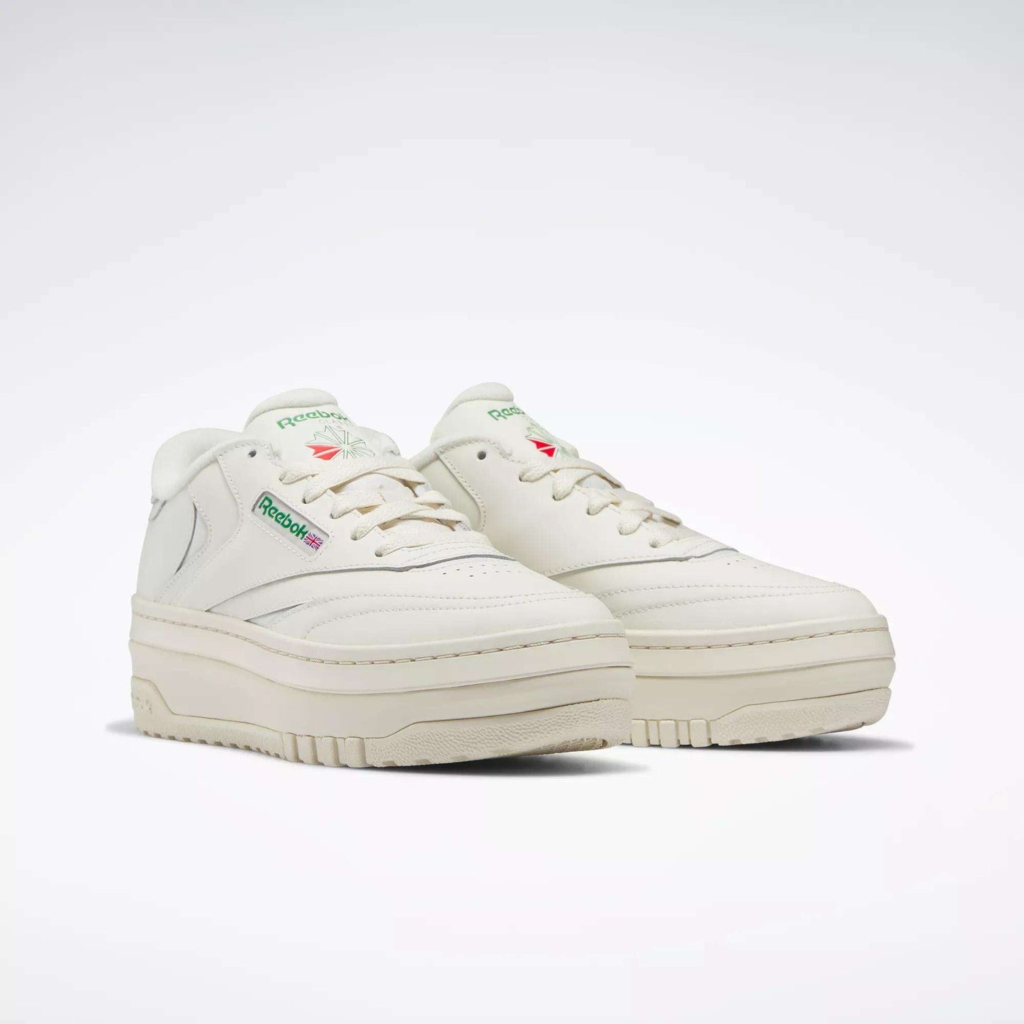 The Women's Club C Extra Shoes by Reebok feature an off-white design, a chunky platform midsole, green branding on the side, and subtle red and green accents. They’re displayed against a plain white background.
