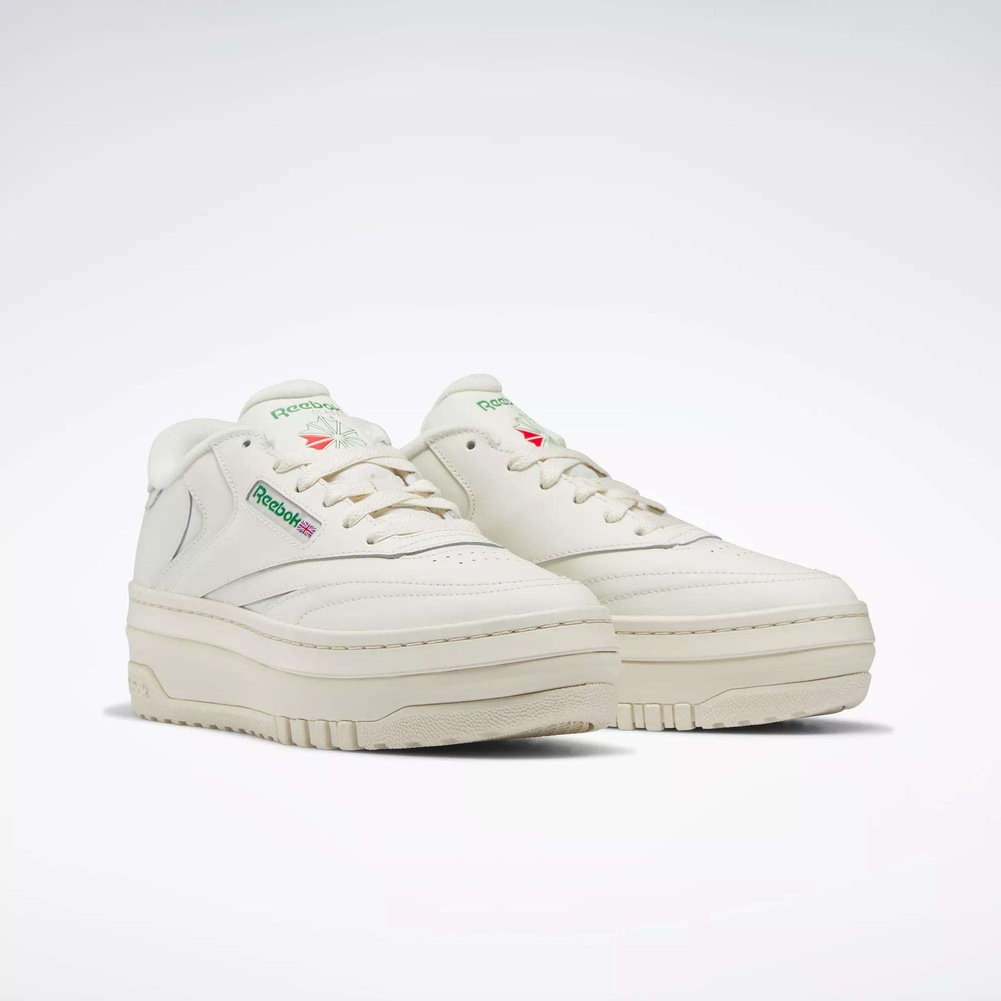 The Women's Club C Extra Shoes by Reebok feature an off-white design, a chunky platform midsole, green branding on the side, and subtle red and green accents. They’re displayed against a plain white background.