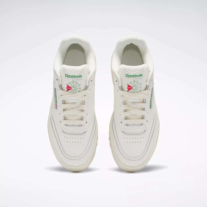 A pair of Reebok Women's Club C Extra Shoes in white, featuring green and pink logo accents and platform midsoles, are shown side by side from above on a plain light background, highlighting the tops, tongues, and laces.