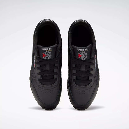 A pair of Reebok Classic Leather Shoes - Big Kids is seen from above, displaying the black uppers and logos on the tongues against a plain light gray background.