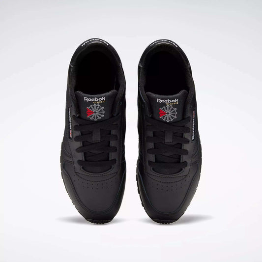 A pair of Reebok Classic Leather Shoes - Big Kids is seen from above, displaying the black uppers and logos on the tongues against a plain light gray background.