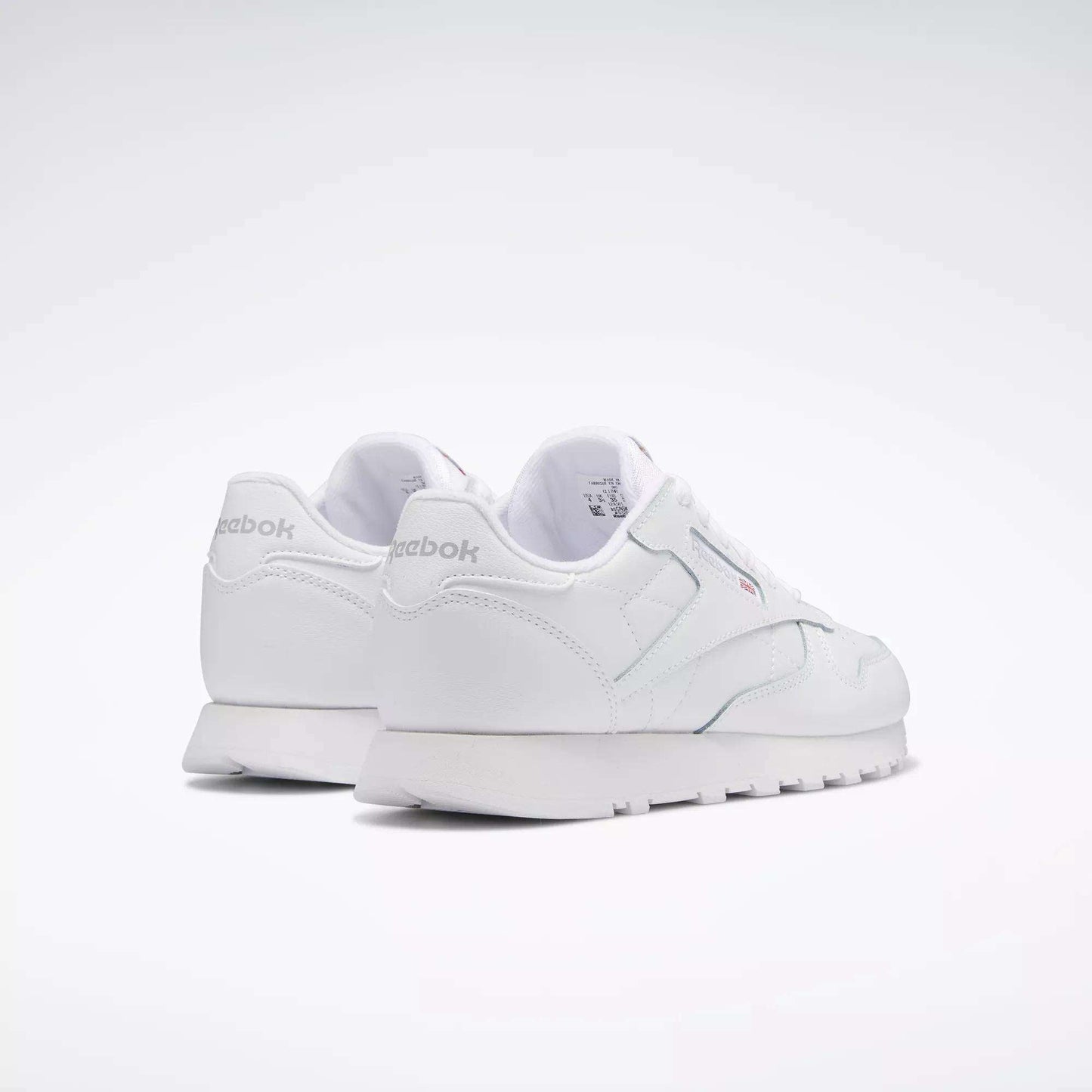 A pair of Reebok Classic Leather Shoes for big kids, shown from the rear on a plain light background. These white sneakers feature a minimal, classic design with the Reebok logo visible on the heel and side.