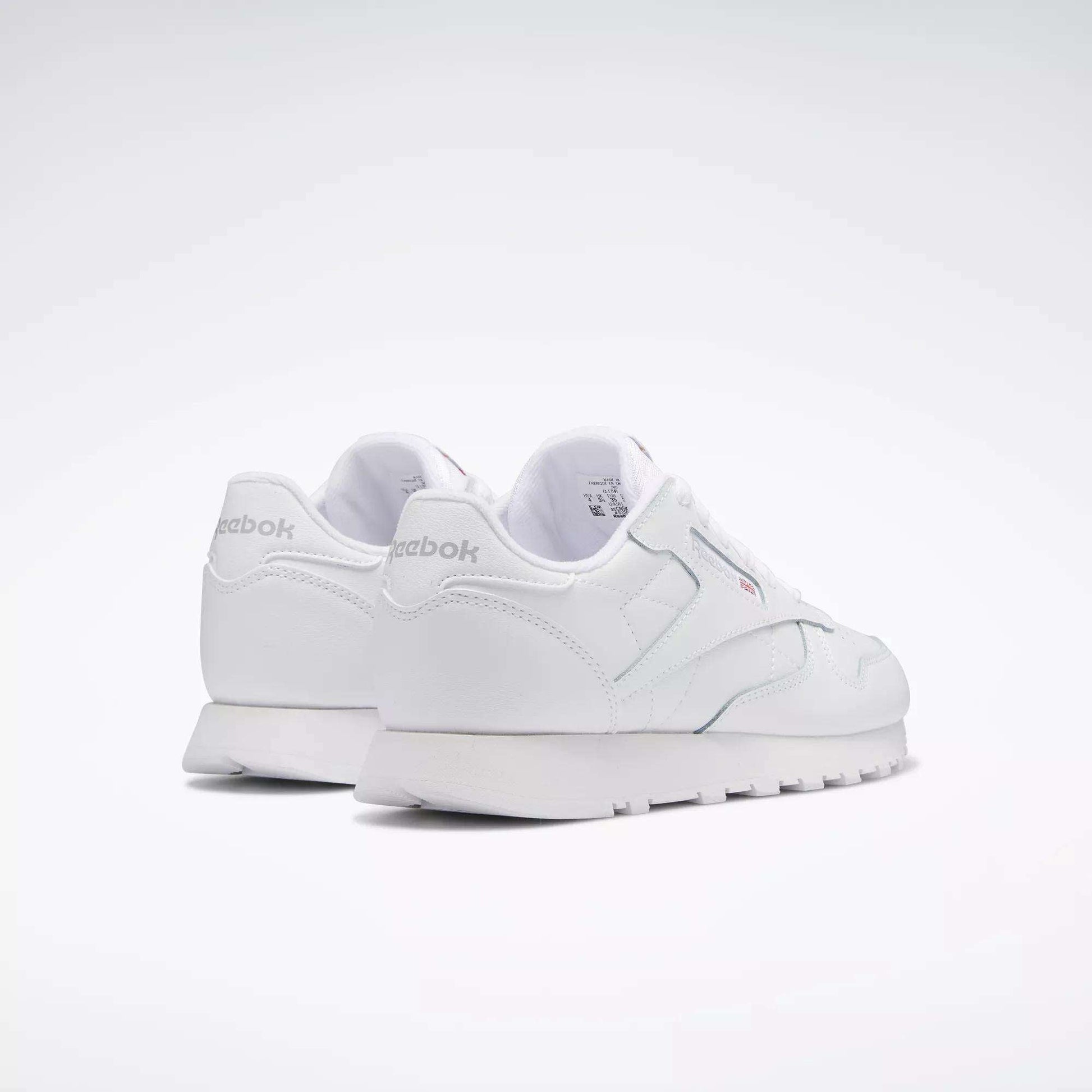 A pair of Reebok Classic Leather Shoes for big kids, shown from the rear on a plain light background. These white sneakers feature a minimal, classic design with the Reebok logo visible on the heel and side.