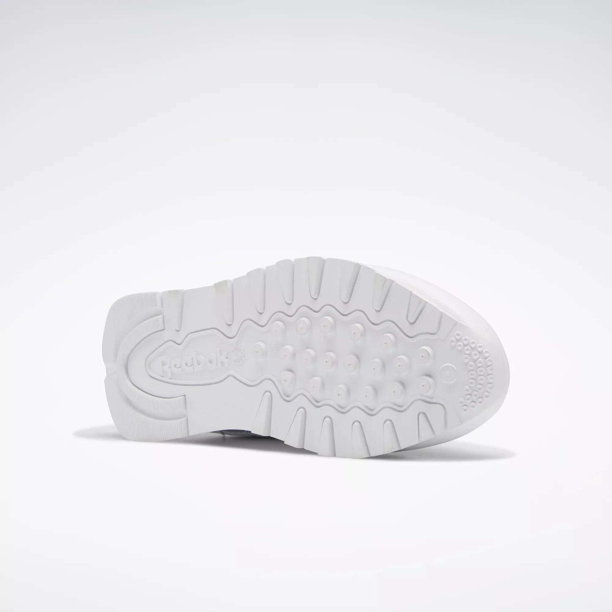 The image displays the white rubber outsole of Reebok Classic Leather Shoes for Big Kids, showing textured grip patterns and the embossed Reebok logo near the heel. The shoe is positioned on its side against a plain, light background.