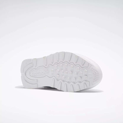 The image displays the white rubber outsole of Reebok Classic Leather Shoes for Big Kids, showing textured grip patterns and the embossed Reebok logo near the heel. The shoe is positioned on its side against a plain, light background.