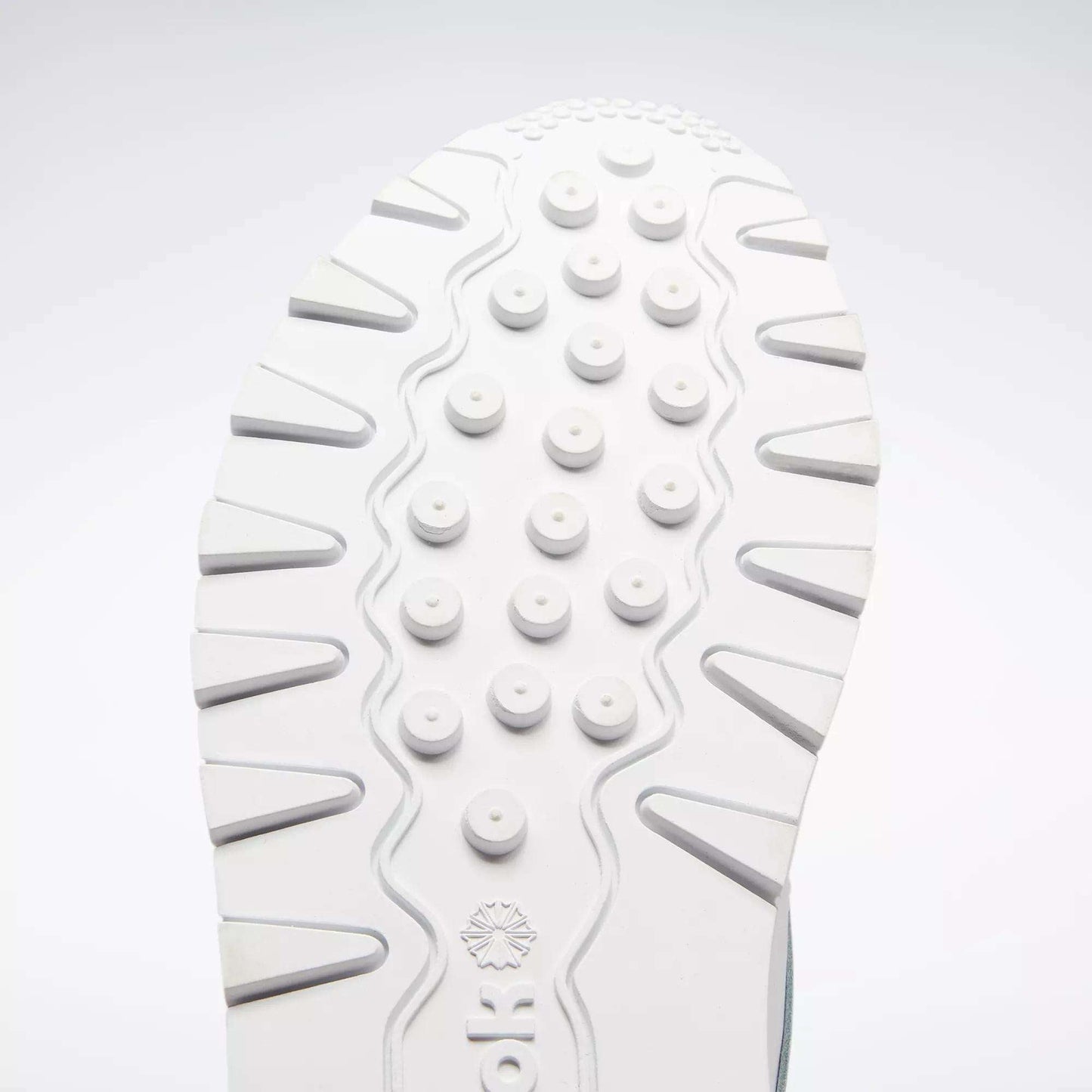 Close-up of a white sole from the Reebok Classic Leather Shoes - Big Kids, featuring round raised bumps and wavy grooves for traction. The classic design stands out against a light gray background, ideal for junior boys.