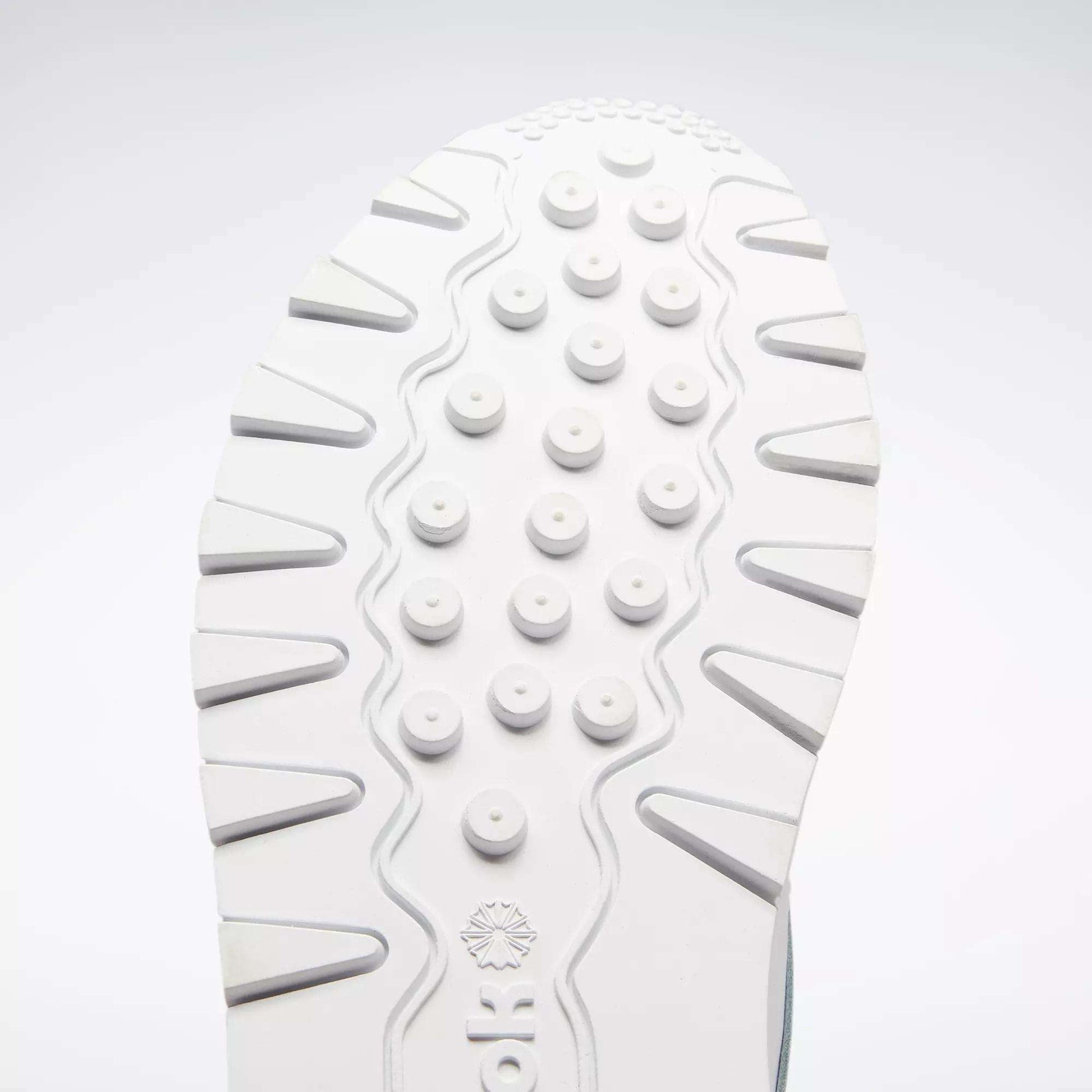 Close-up of a white sole from the Reebok Classic Leather Shoes - Big Kids, featuring round raised bumps and wavy grooves for traction. The classic design stands out against a light gray background, ideal for junior boys.