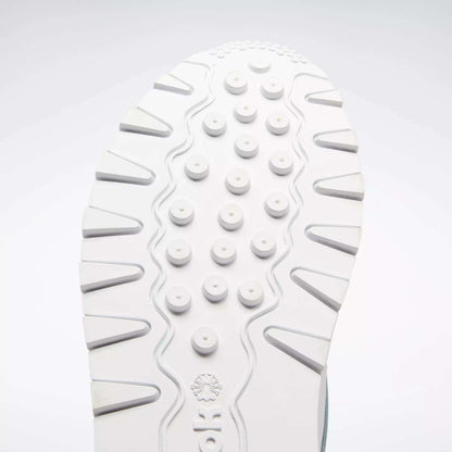 Close-up of a white sole from the Reebok Classic Leather Shoes - Big Kids, featuring round raised bumps and wavy grooves for traction. The classic design stands out against a light gray background, ideal for junior boys.