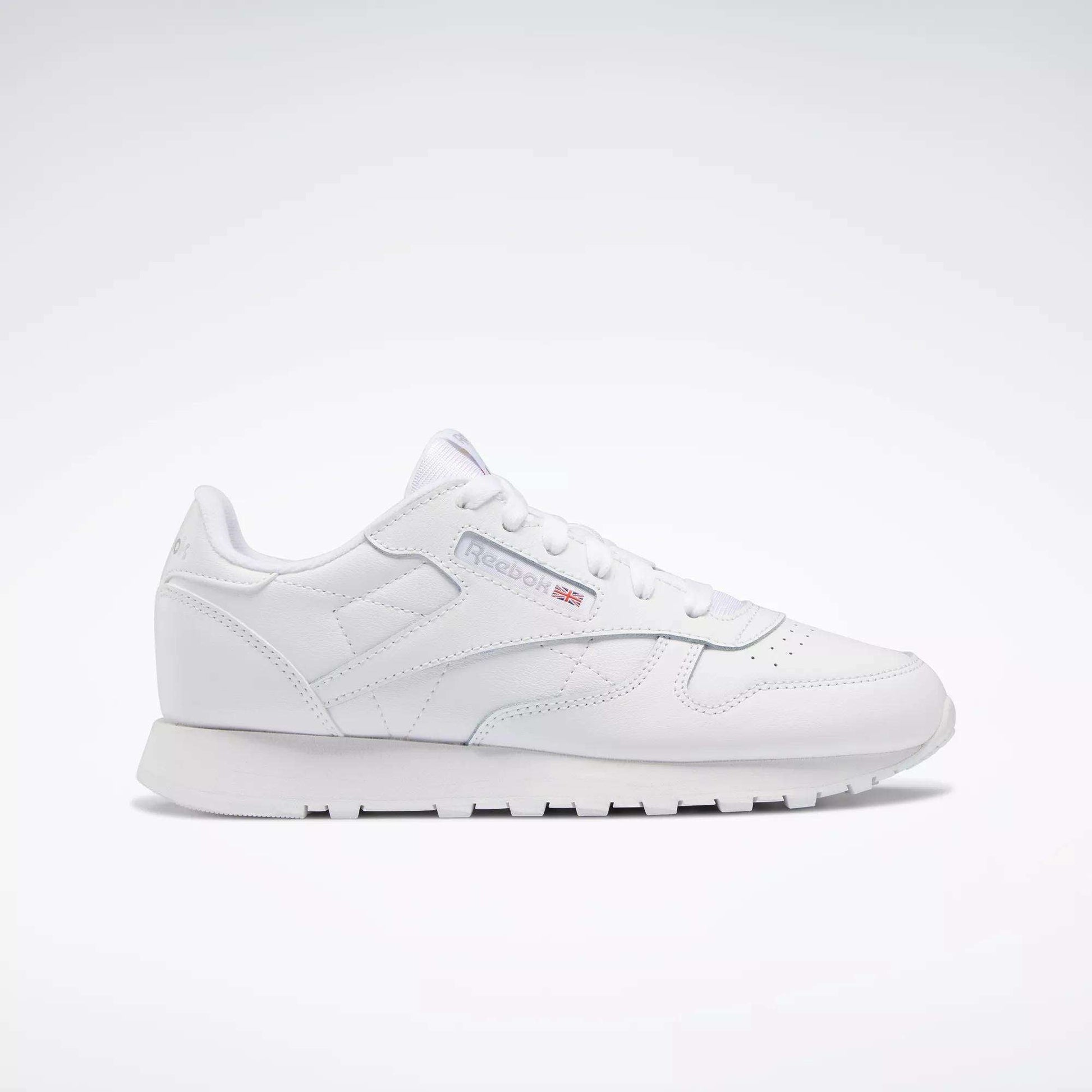 The Reebok Classic Leather Shoes - Big Kids feature an all-white, low-top design with lace-up closure, subtle side branding, and a flat rubber sole—perfect for adding minimalist style to any junior boys' shoe collection.
