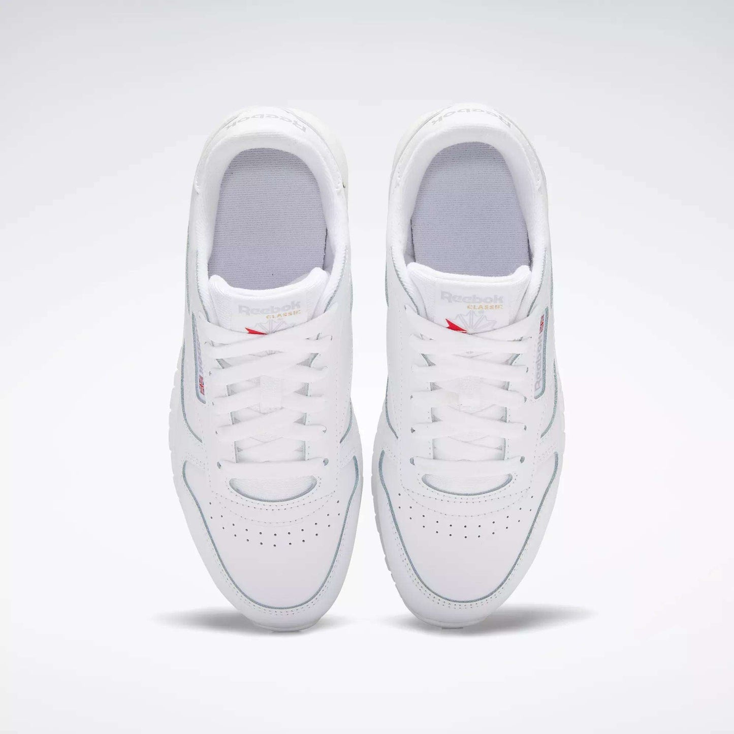 A pair of Reebok Classic Leather Shoes for big kids in white, viewed from above with both shoes side by side, laces tied, and subtle branding on the tongues—a timeless design.