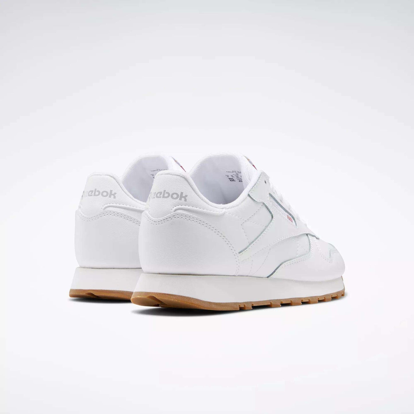 A pair of Reebok Classic Leather Shoes - Big Kids in white with gum soles and a stitched side-stripe, shown from the back and side against a plain light background. The Reebok brand name is visible on the heel.