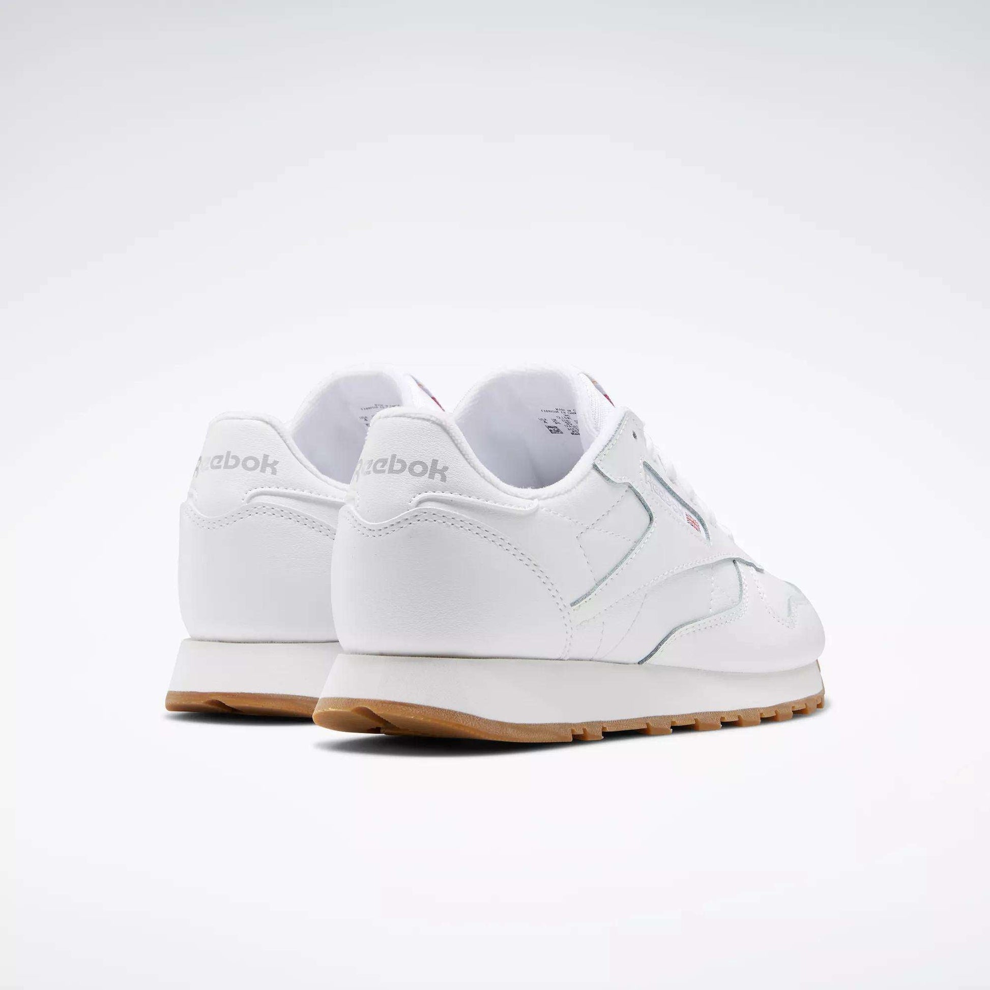 A pair of Reebok Classic Leather Shoes - Big Kids in white with gum soles and a stitched side-stripe, shown from the back and side against a plain light background. The Reebok brand name is visible on the heel.