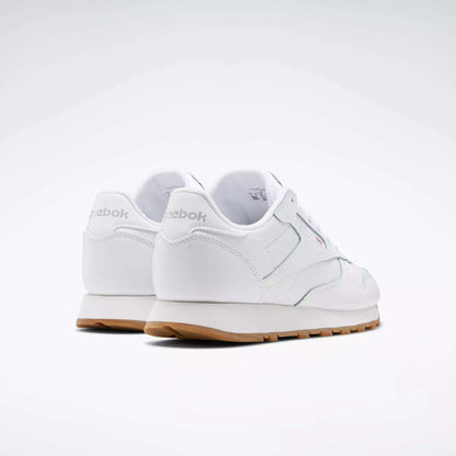 A pair of Reebok Classic Leather Shoes - Big Kids in white with gum soles and a stitched side-stripe, shown from the back and side against a plain light background. The Reebok brand name is visible on the heel.