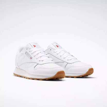 A pair of Reebok Classic Leather Shoes - Big Kids, in white with stitched side-stripe, gum rubber soles, subtle branding, and white laces are placed side by side on a plain white background.