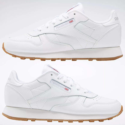Two Reebok Classic Leather Shoes - Big Kids with gum soles and stitched side-stripes are shown side by side on a plain background, displaying both outer and inner views. The Reebok logo and Union Jack appear on the sides.