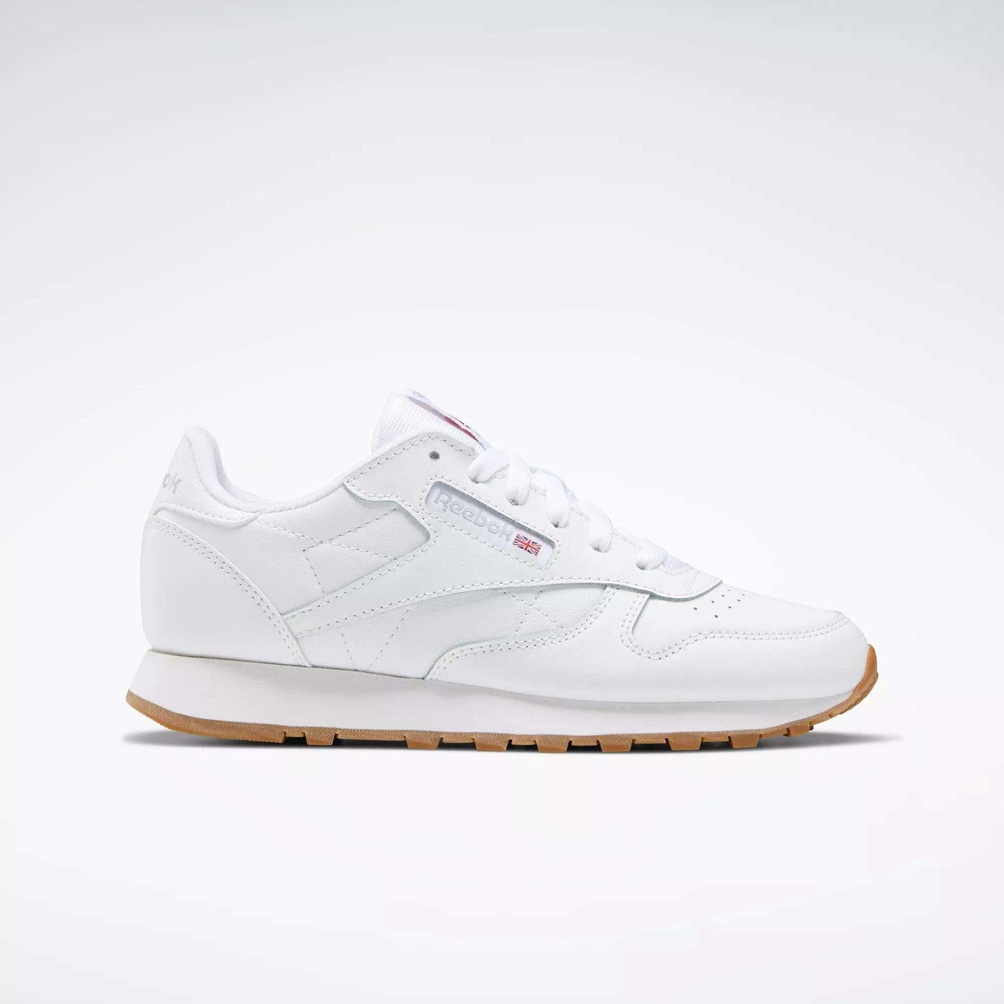 A Reebok Classic Leather Shoes - Big Kids sneaker in white with a gum sole, stitched side-stripe, side logo, and red, white, and blue Reebok emblem is shown from the side against a plain light background.