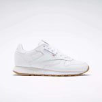 A Reebok Classic Leather Shoes - Big Kids sneaker in white with a gum sole, stitched side-stripe, side logo, and red, white, and blue Reebok emblem is shown from the side against a plain light background.