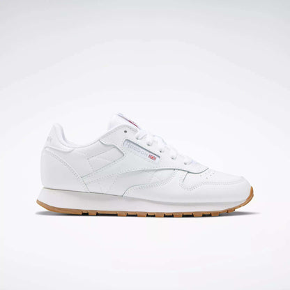 A Reebok Classic Leather Shoes - Big Kids sneaker in white with a gum sole, stitched side-stripe, side logo, and red, white, and blue Reebok emblem is shown from the side against a plain light background.