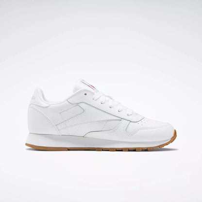 The Reebok Classic Leather Shoes - Big Kids feature a white leather upper, classic stitched side-stripe, white laces and sole, plus a light brown rubber outsole. Shown in side profile against a plain background. Ideal for junior boys' shoe collections.