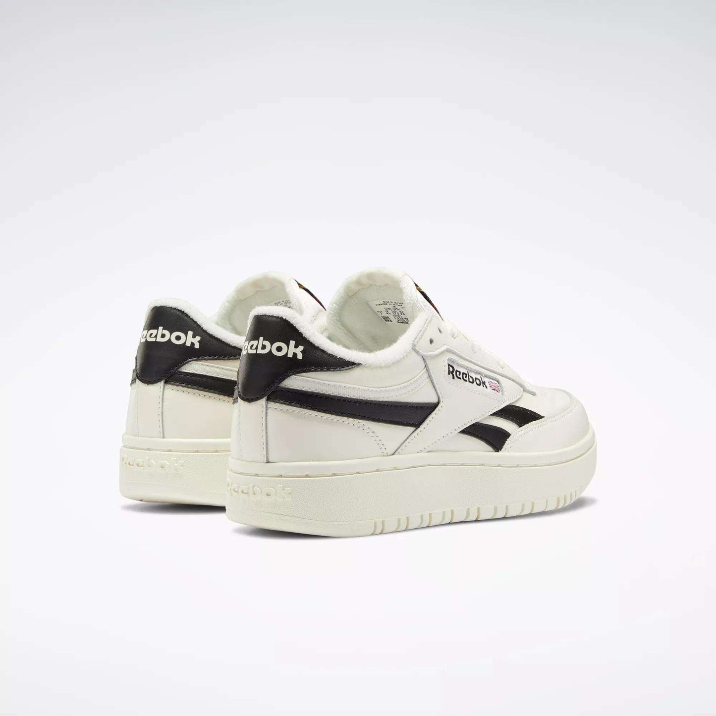 A pair of Reebok Women's Club C Double Revenge Shoes, featuring black accents and logo with a double outsole for style, are arranged side by side on a light background. The left shoe turns outward, highlighting the Reebok heel branding.