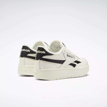 A pair of Reebok Women's Club C Double Revenge Shoes, featuring black accents and logo with a double outsole for style, are arranged side by side on a light background. The left shoe turns outward, highlighting the Reebok heel branding.