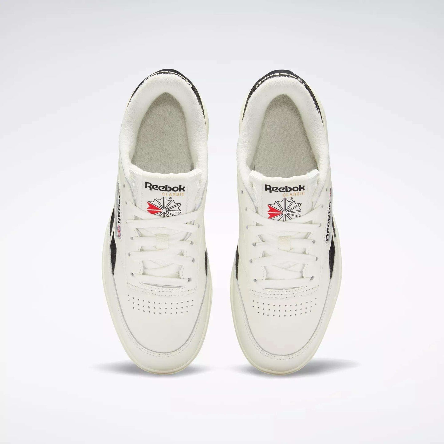 Top-down view of Women's Club C Double Revenge Shoes by Reebok, featuring black accents, double outsole, Reebok logos on the tongue, and perforated toe area, displayed side by side on a light background.