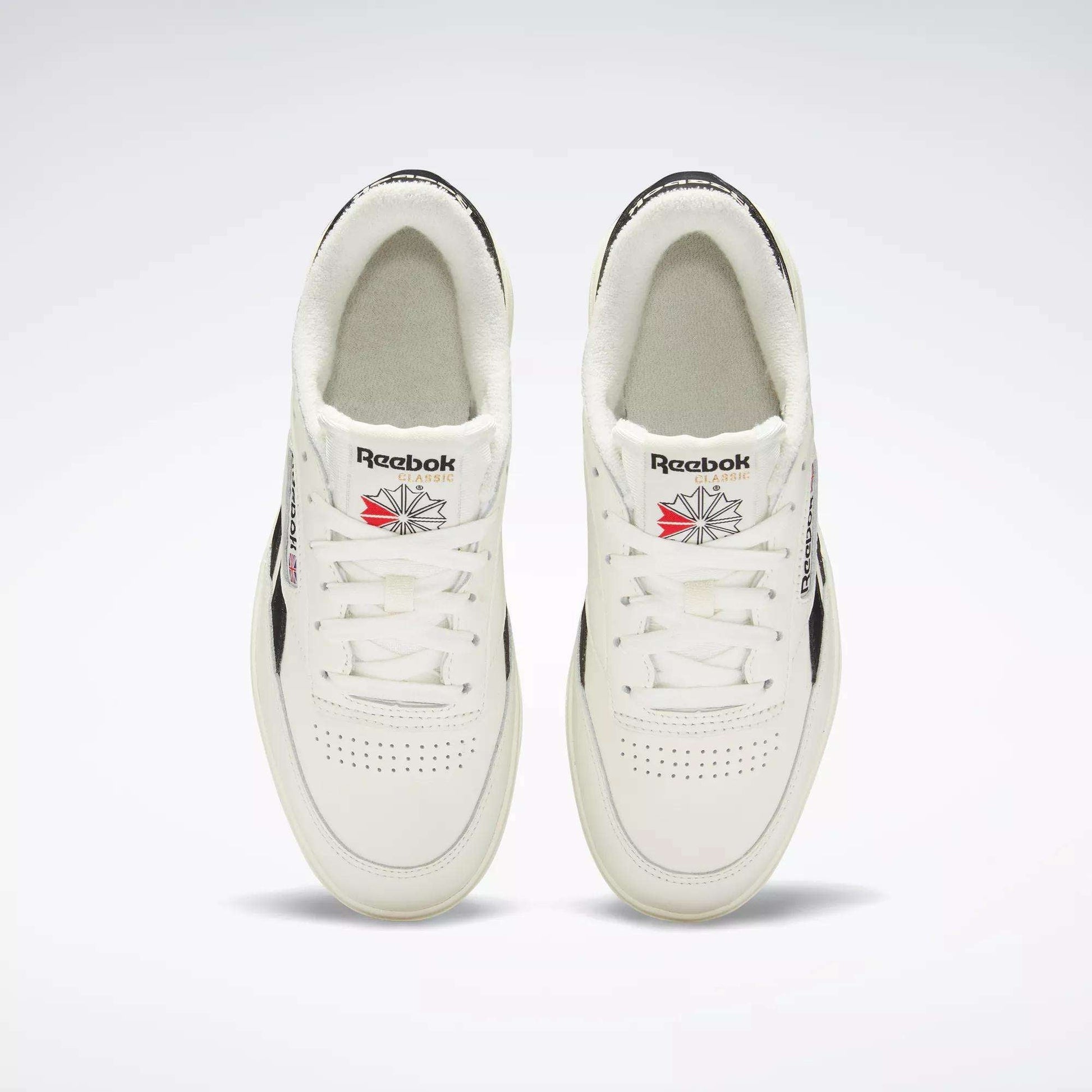 Top-down view of Women's Club C Double Revenge Shoes by Reebok, featuring black accents, double outsole, Reebok logos on the tongue, and perforated toe area, displayed side by side on a light background.