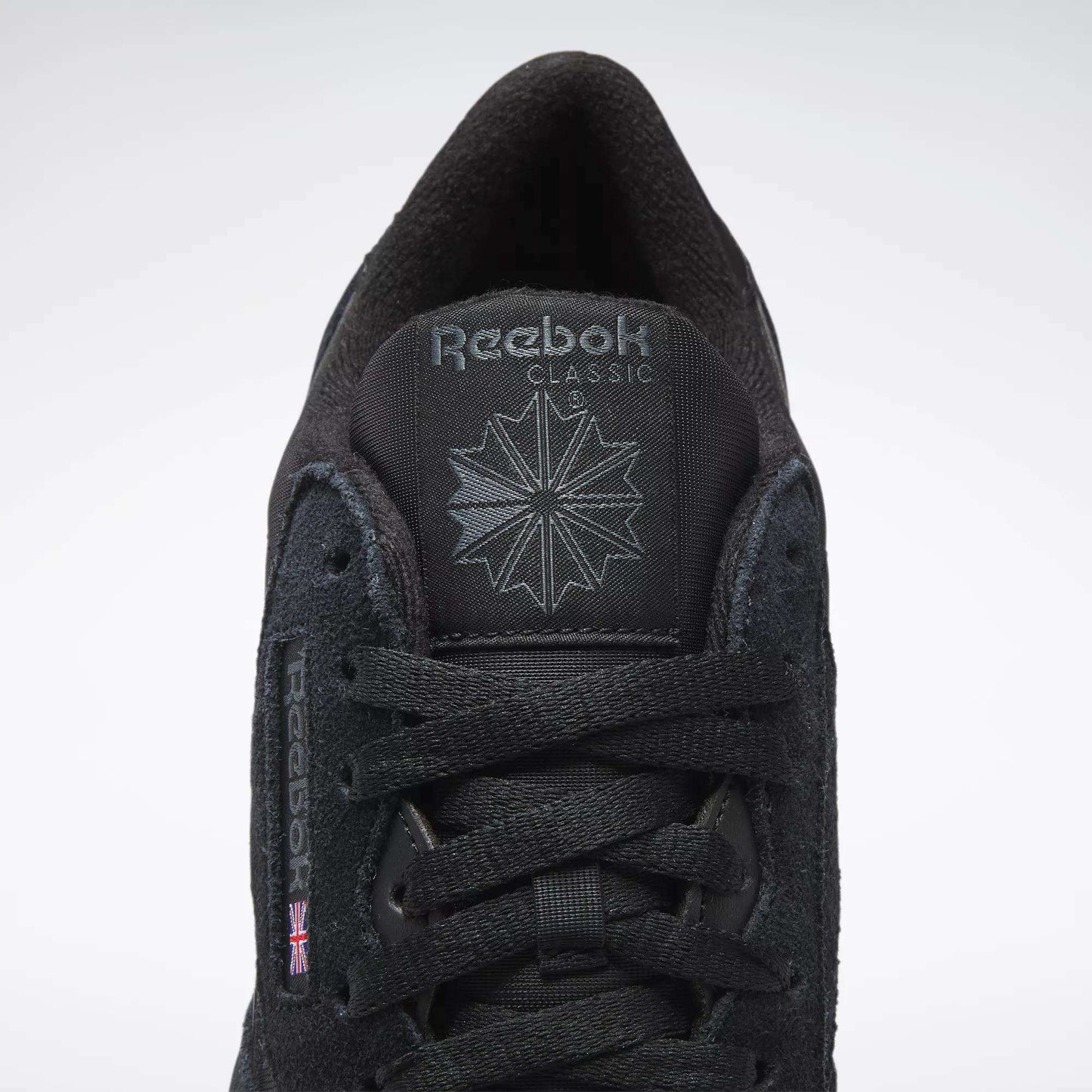 A close-up of Reebok Men's Classic Nylon Shoes features a black nylon upper, black laces, Reebok logo and starburst on the tongue, and a small UK flag on the side—timeless sneakers from Reebok.