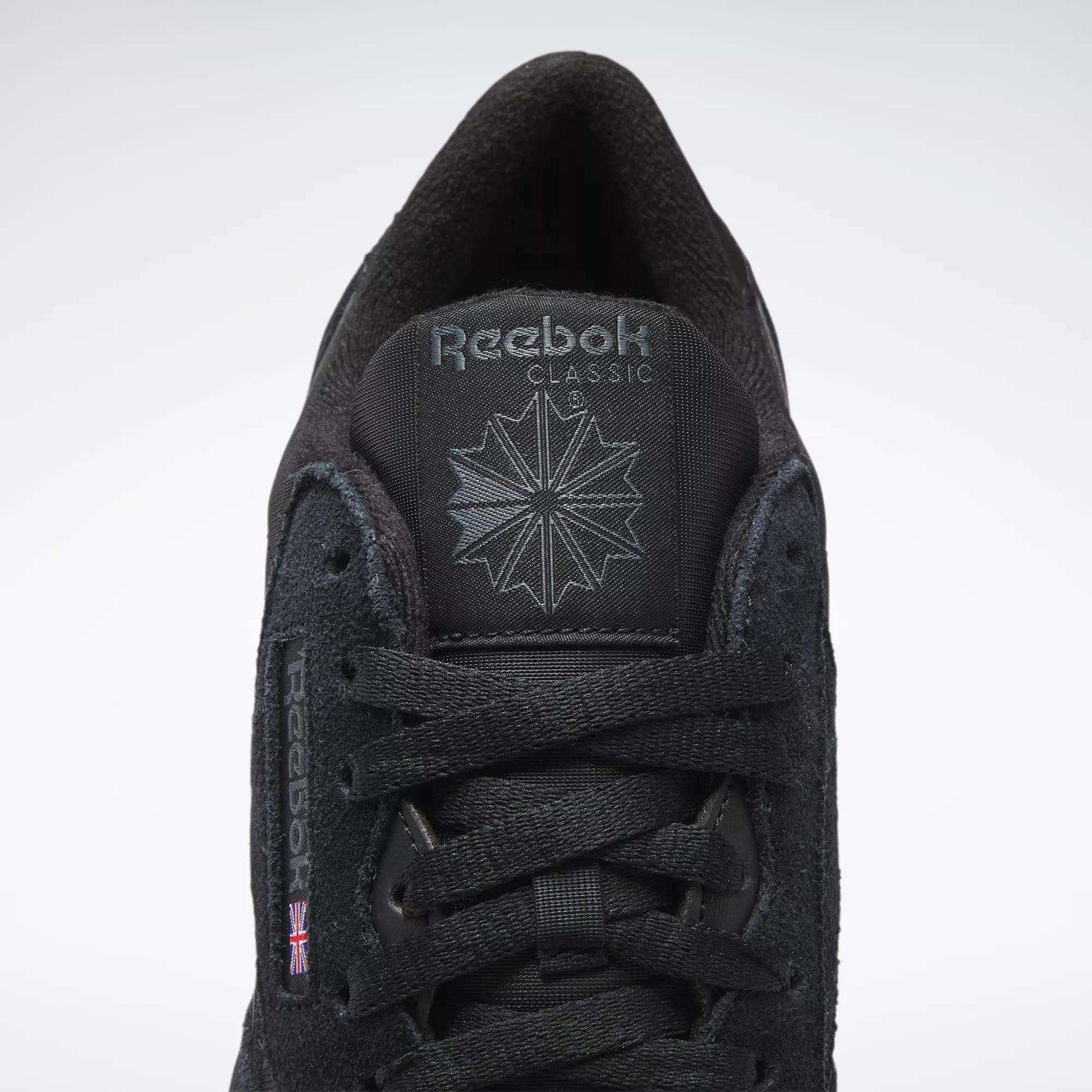 A close-up of Reebok Men's Classic Nylon Shoes features a black nylon upper, black laces, Reebok logo and starburst on the tongue, and a small UK flag on the side—timeless sneakers from Reebok.