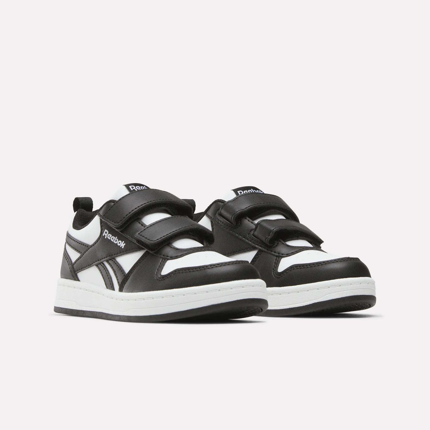 A pair of Kids' Reebok Royal Prime 2 Shoes for little kids, featuring black and white design, two hook-and-loop straps, white soles, and the Reebok logo on the side and tongue, shown against a plain white background.