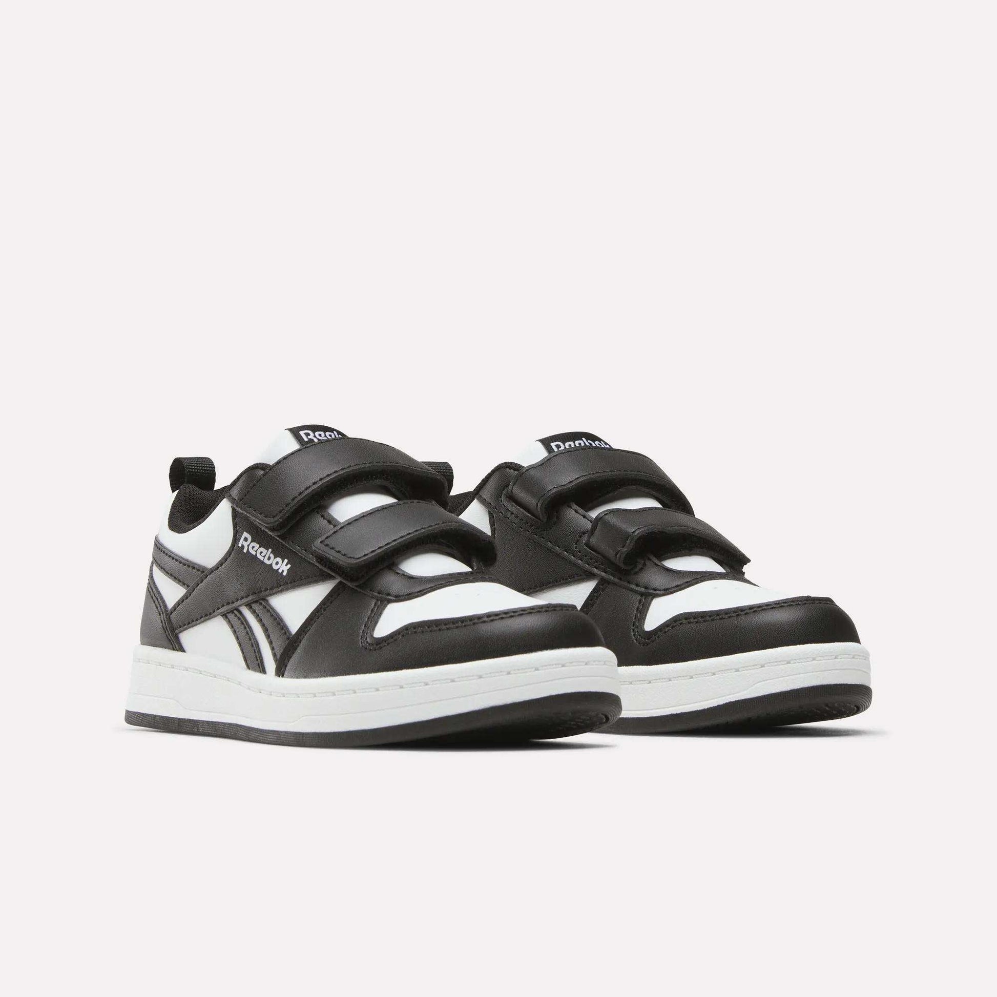 A pair of Kids' Reebok Royal Prime 2 Shoes for little kids, featuring black and white design, two hook-and-loop straps, white soles, and the Reebok logo on the side and tongue, shown against a plain white background.