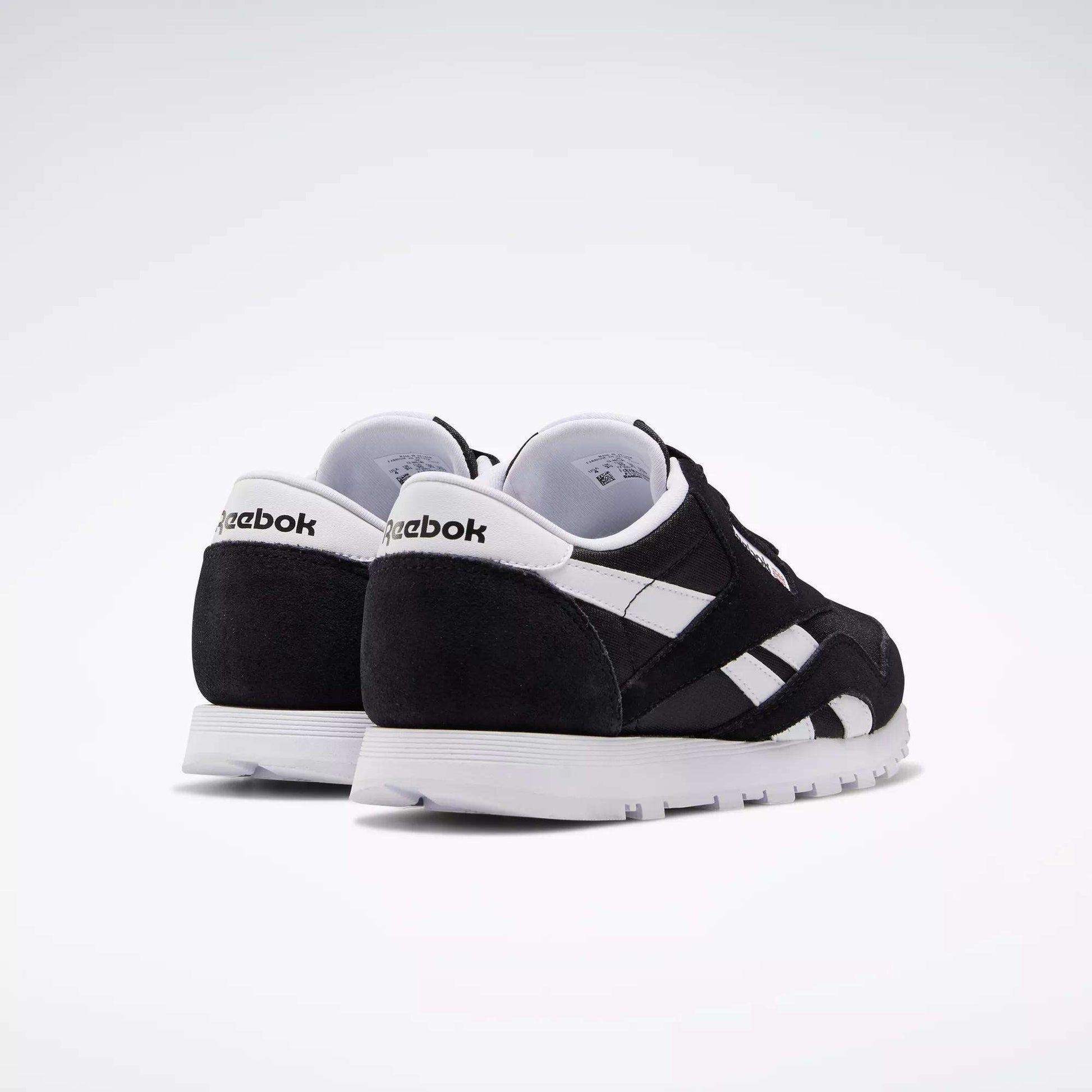 A pair of Reebok Classic Nylon Shoes - Big Kids are angled on a white background to show the back and side views, featuring black and white colors, crisp white soles, and the iconic Reebok logo.