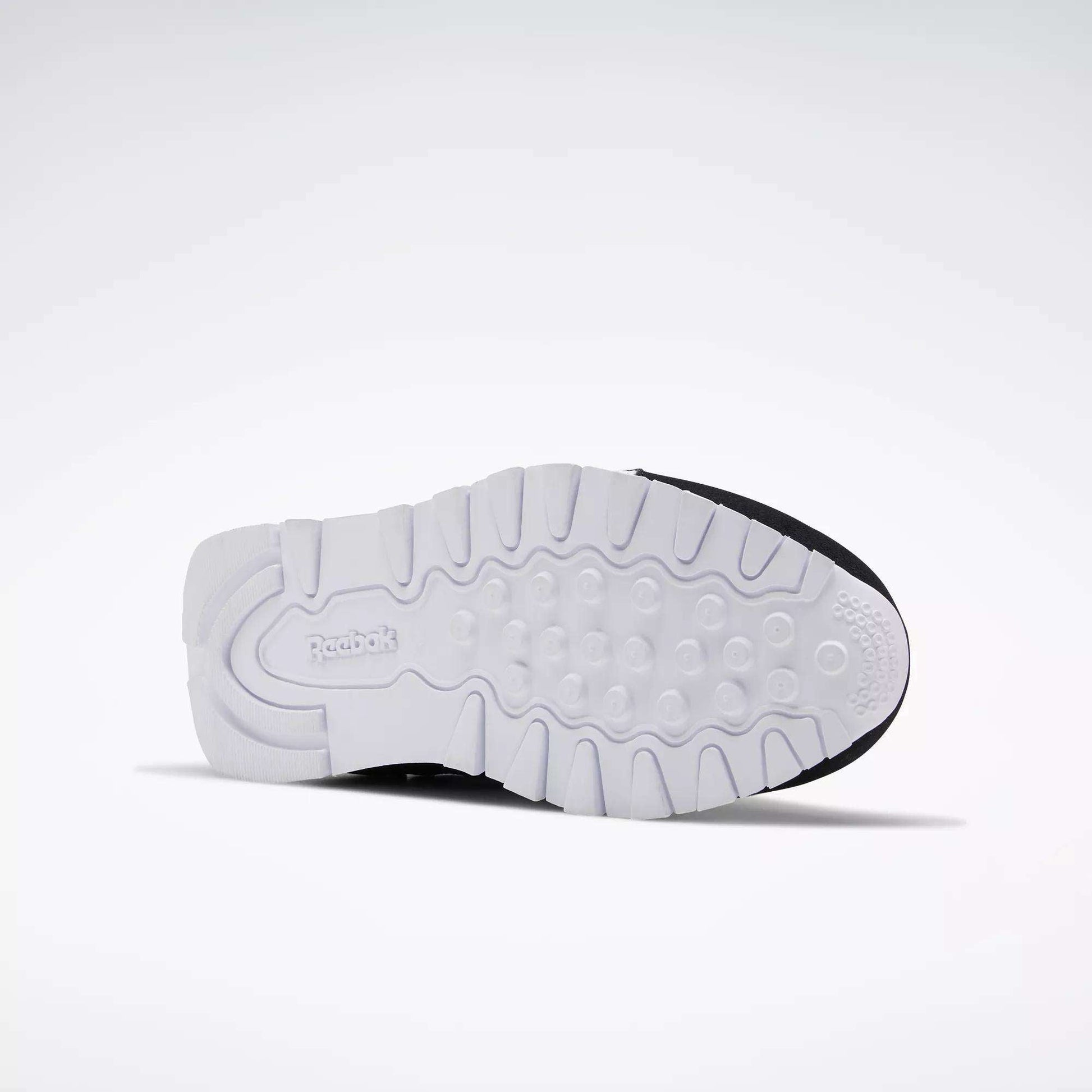 The image displays the sole of Reebok Classic Nylon Shoes - Big Kids facing upward, featuring a white, textured grip pattern and the Reebok logo by the heel. Its minimalist design pays tribute to classic 80s styles against a plain light gray background.